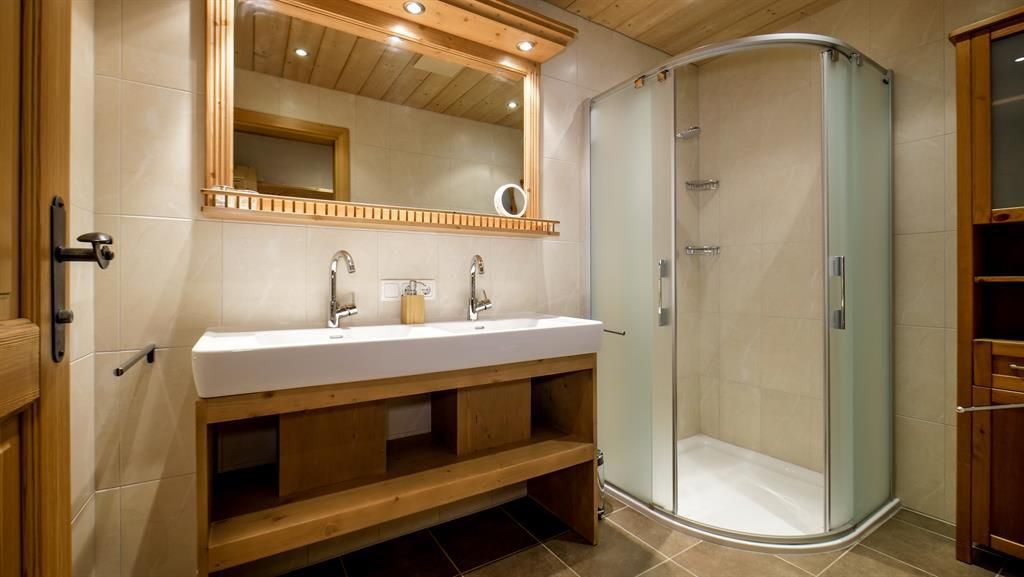 A modern bathroom with a bright vanity and two sinks. On the right side, there is a shower with a glass door.