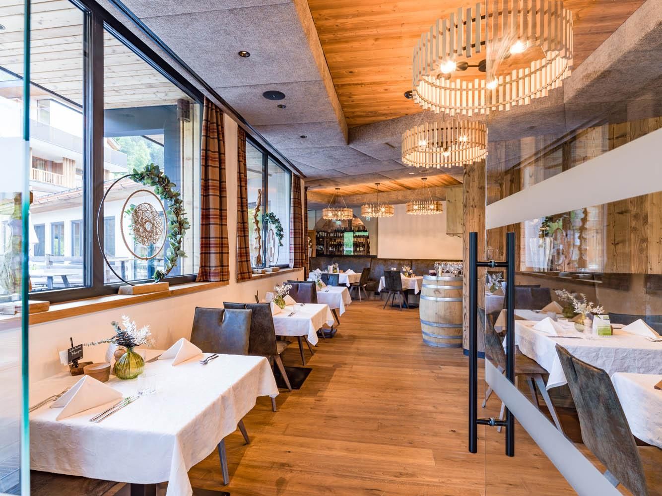 A cozy restaurant with wooden flooring and stylish tables. Large windows provide plenty of daylight and a view of the surroundings.