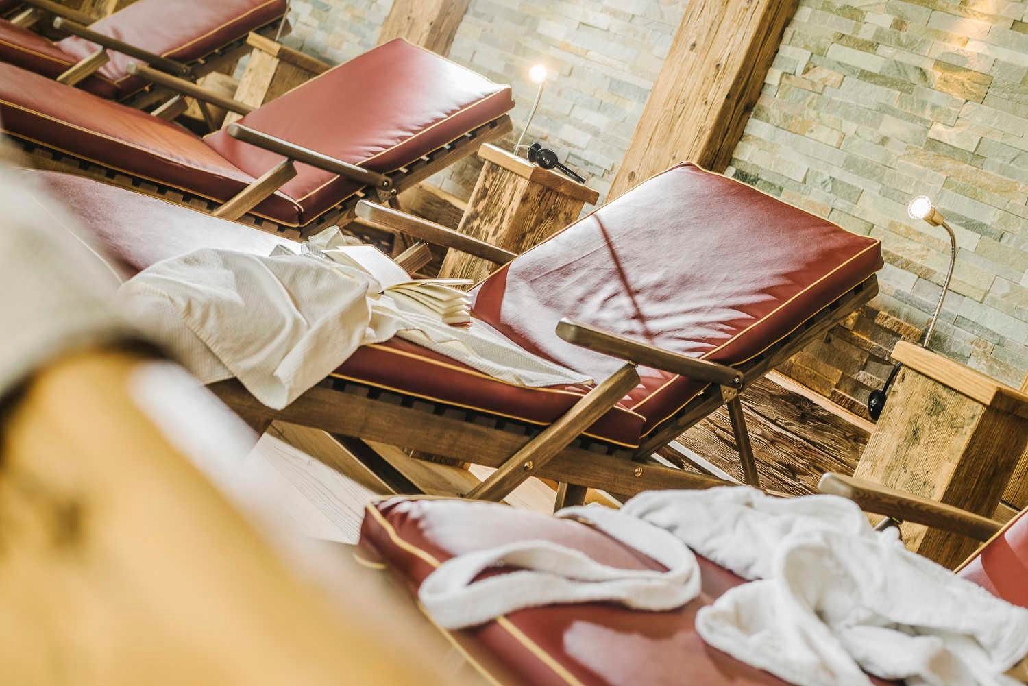 A relaxing room with comfortable lounges and white towels. The walls are made of wood and stone, creating a cozy atmosphere.