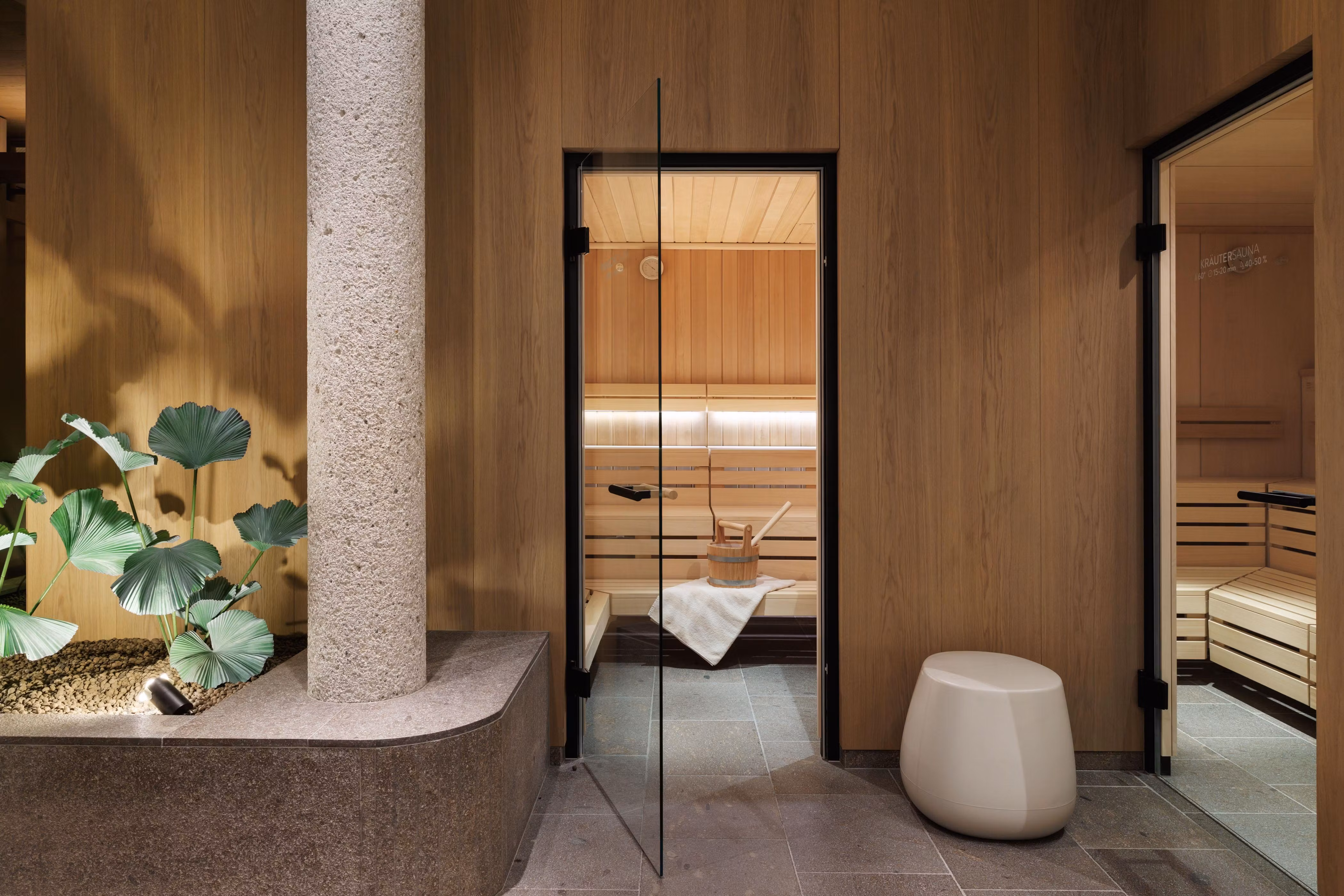 A modern wellness area with a sauna and a minimally designed room. A green plant arrangement and bright wood walls create a relaxing atmosphere.
