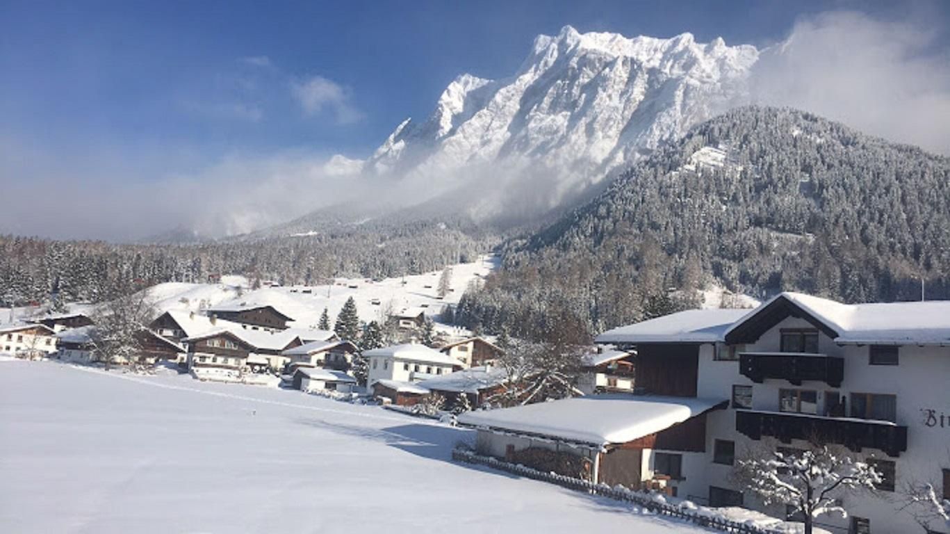 A picturesque winter landscape with snow-covered mountains and a tranquil village. The houses are surrounded by snow and it radiates a peaceful atmosphere.