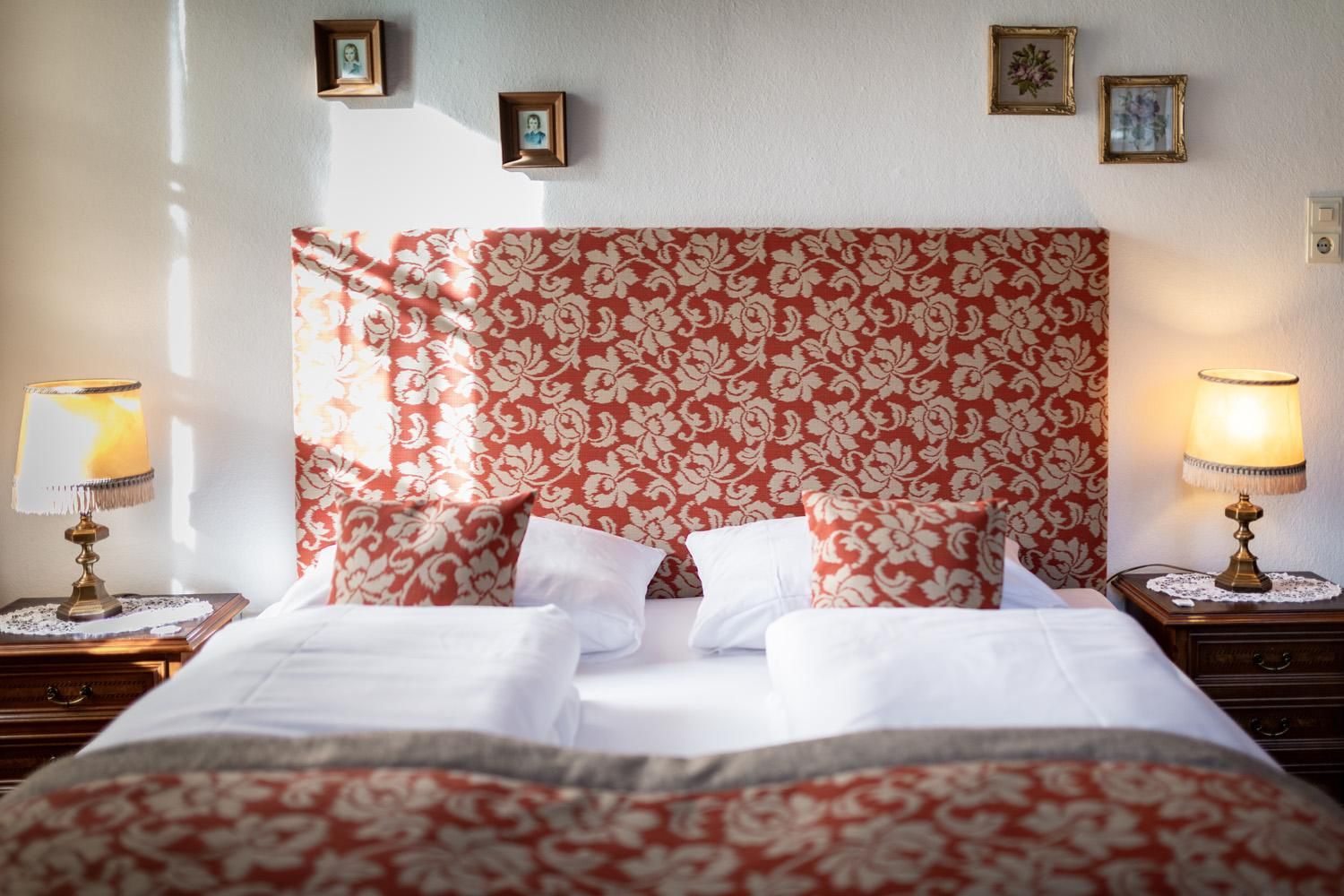 An inviting bedroom with a beautiful red headboard and cozy bed pillows. Two lamps and decorative pictures give the room a cozy atmosphere.