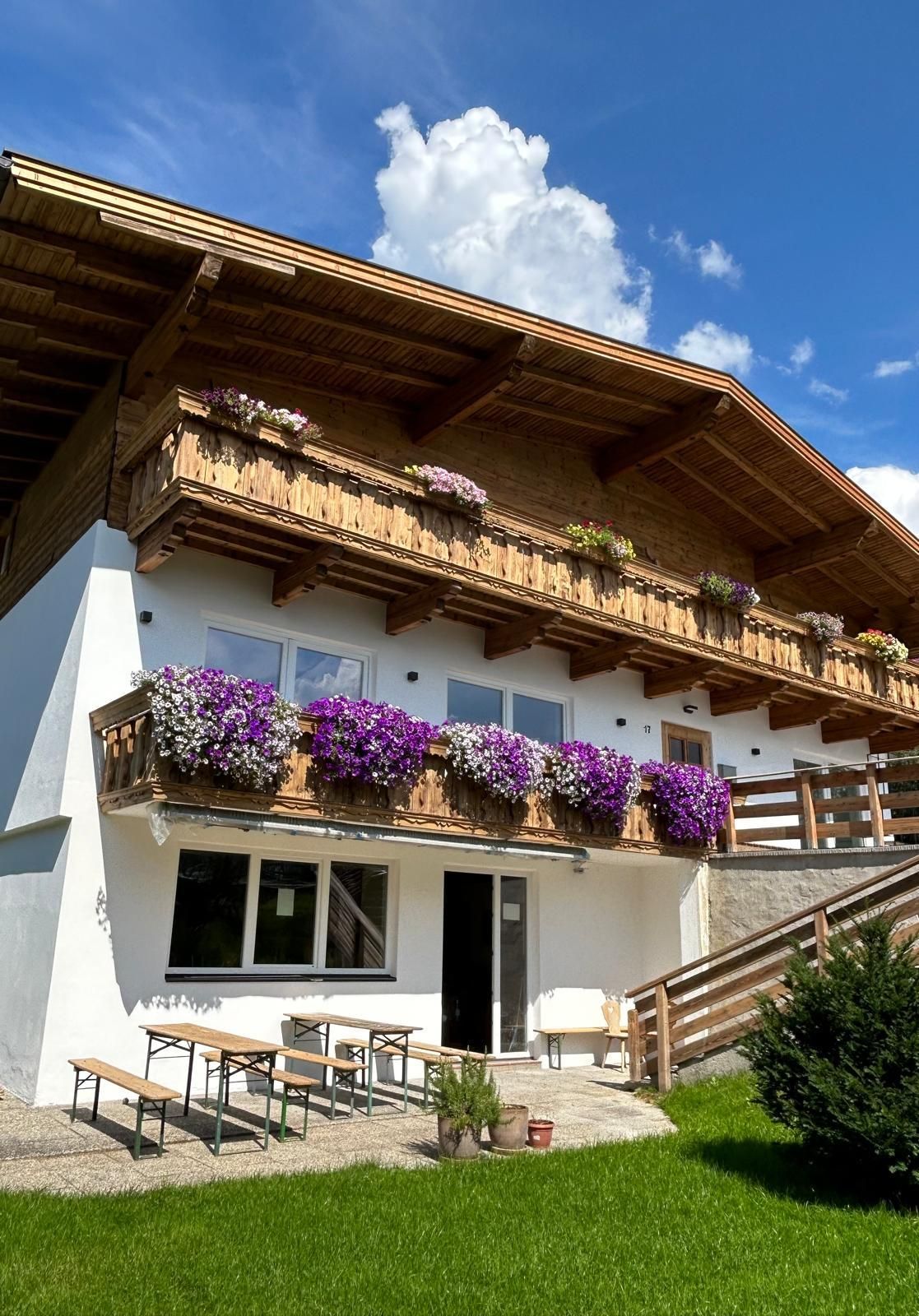 A charming house with flowers on the balconies. The sky is blue and there is plenty of green space all around.