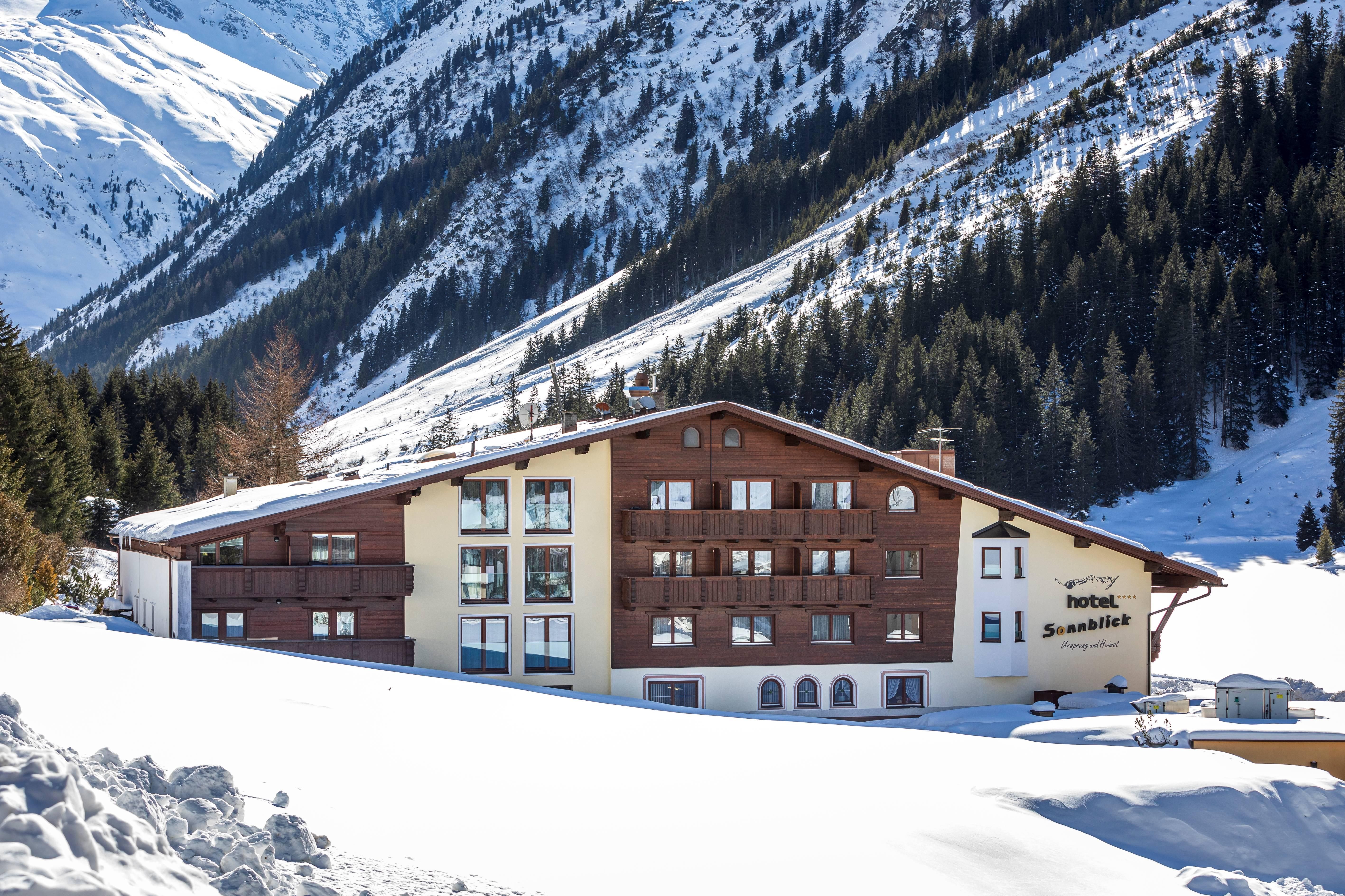 A stylish hotel amidst a snowy mountain landscape. The surroundings are characterized by tall firs and majestic mountains.