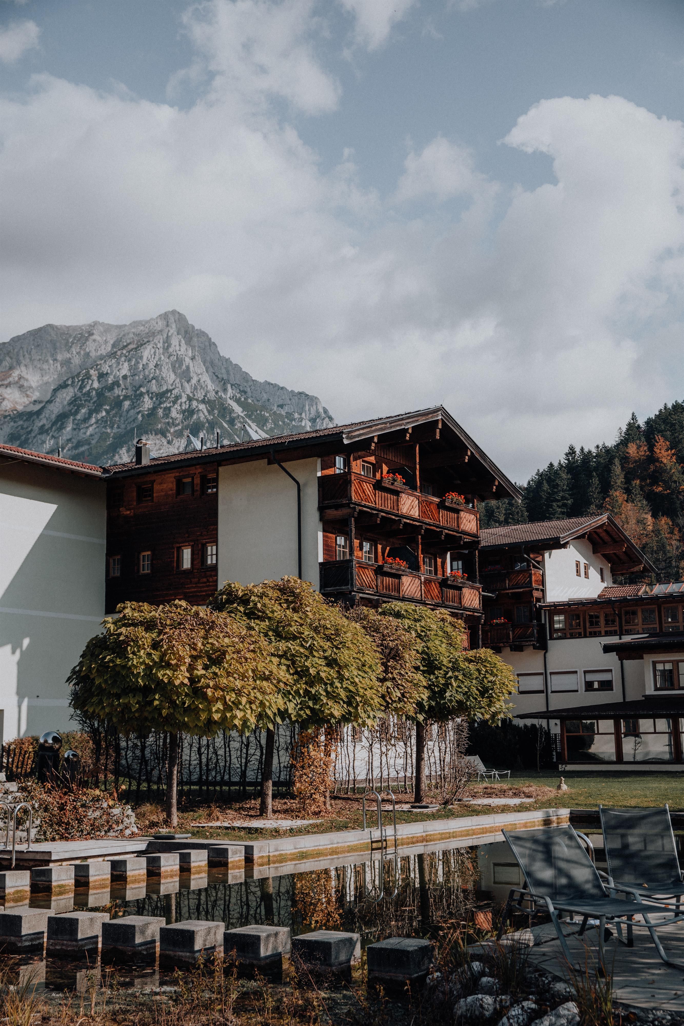 A picturesque building in the mountains with autumn trees and a tranquil pond. The landscape is surrounded by an impressive mountain backdrop.