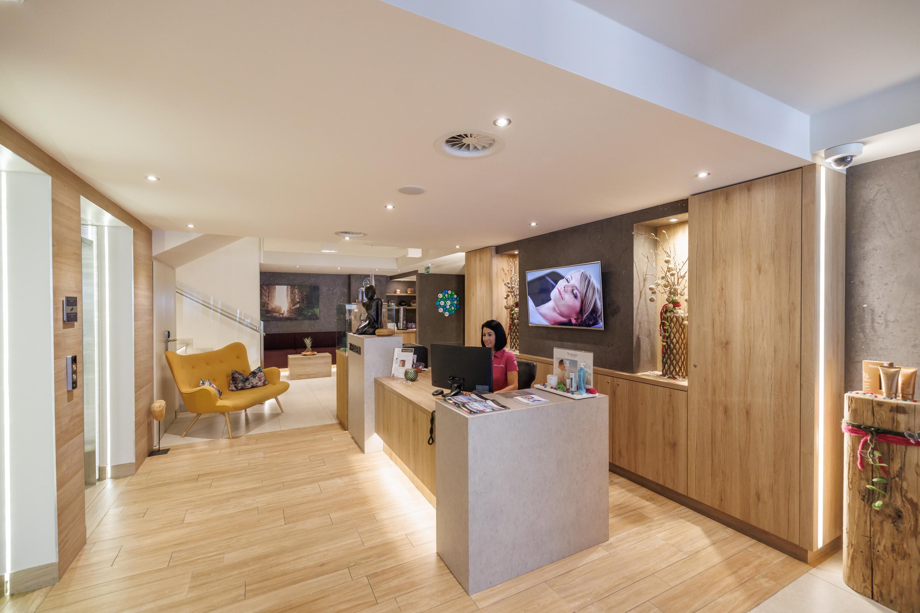 A modern reception area with wooden paneling and cozy seating. An employee stands at the reception desk and greets the guests.