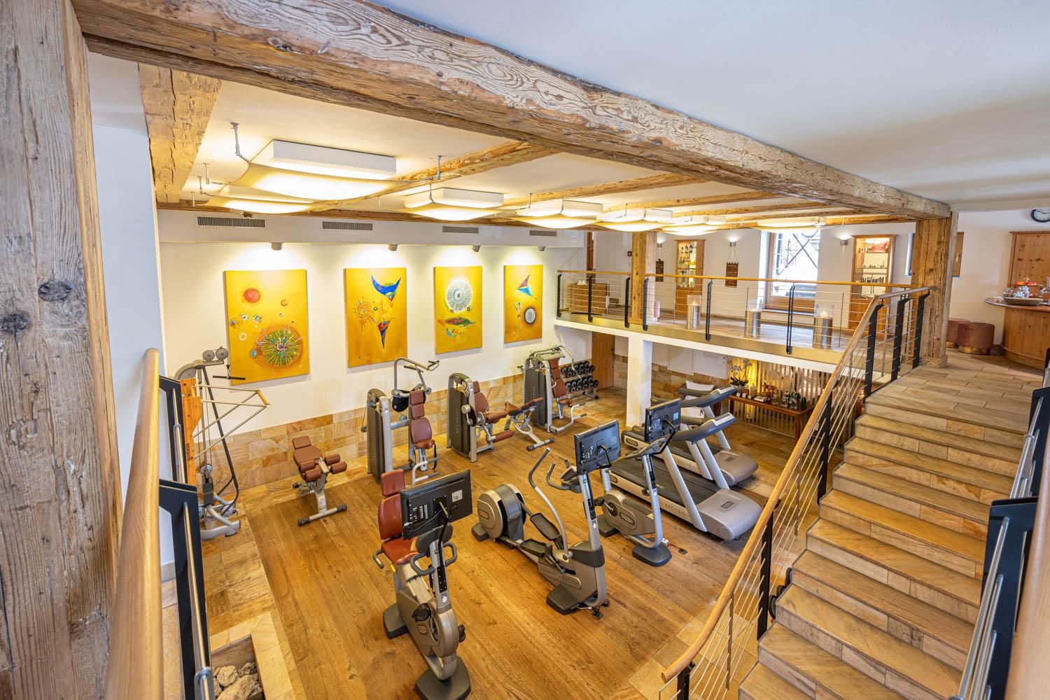 A modern gym with various equipment and appealing artworks on the walls. The space has an open and airy character with wooden paneling.