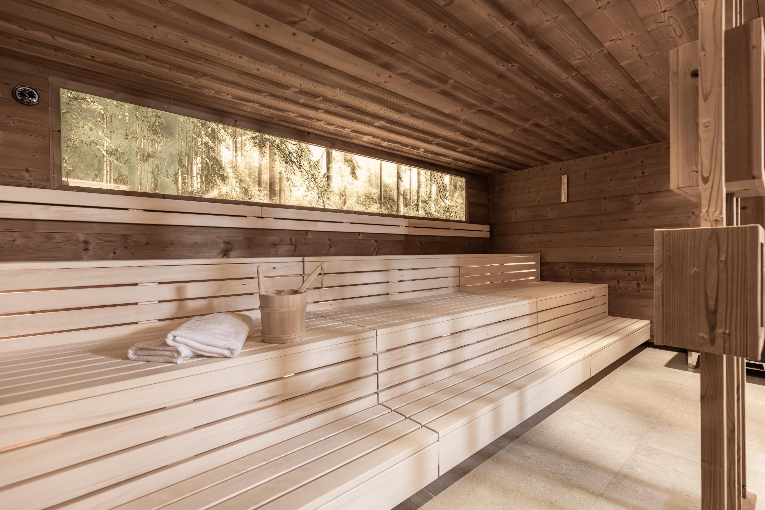 A bright sauna room with a wooden bench and large windows. Towels are ready for relaxing hours.