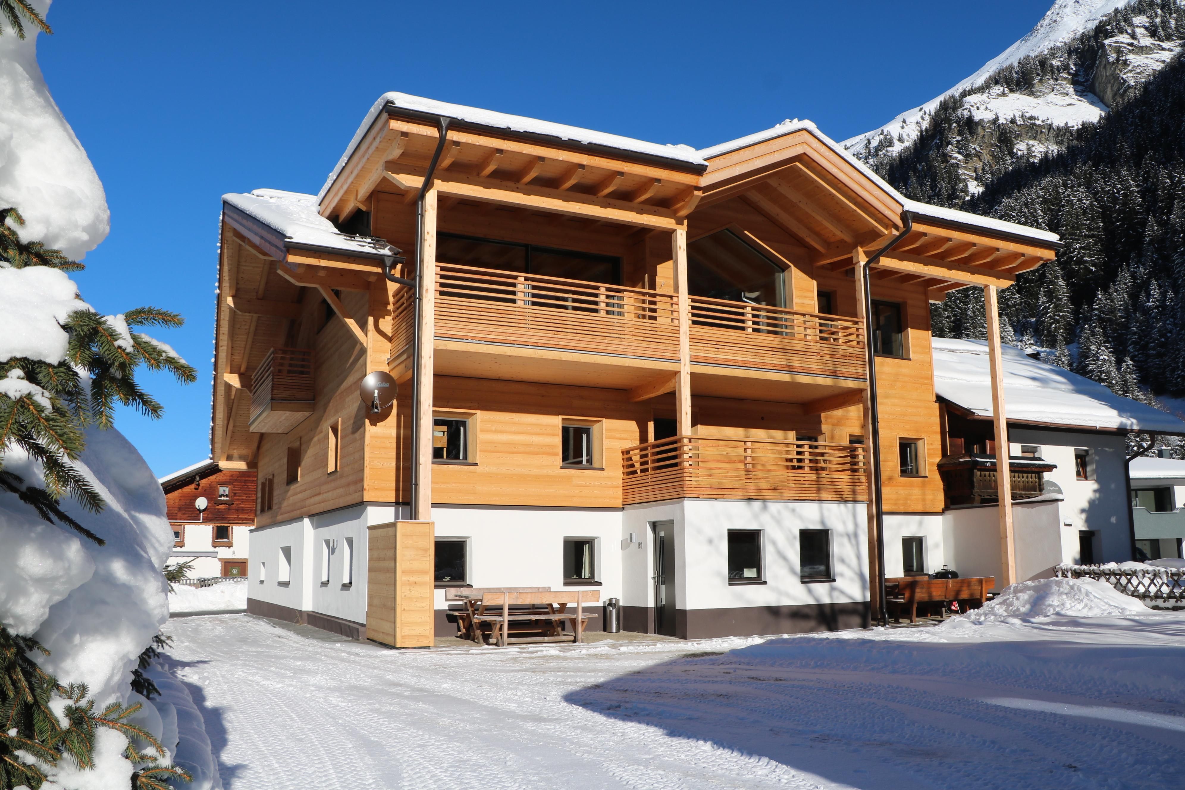 A modern wooden house in a snow-covered landscape. The crisp winter air and the mountains in the background create a cozy atmosphere.