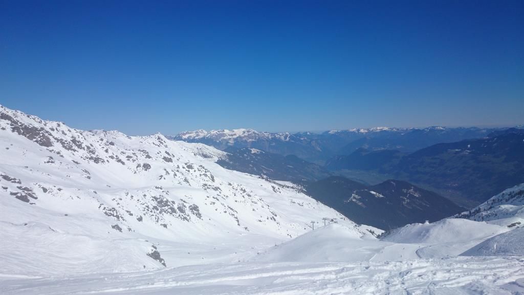 A snow-covered mountain landscape under a clear blue sky. The view shows majestic mountains in the distance.