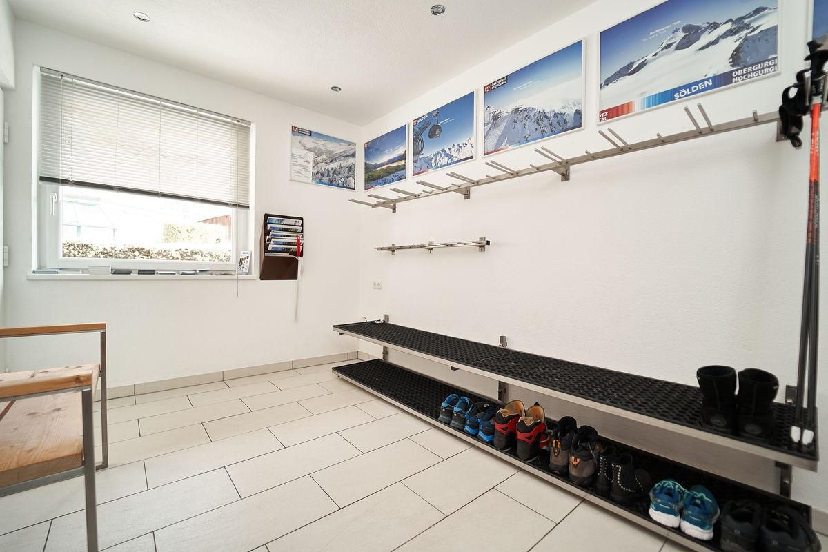 A practical ski room with shoe racks and a bench. On the walls, there are pictures of mountains and ski areas.