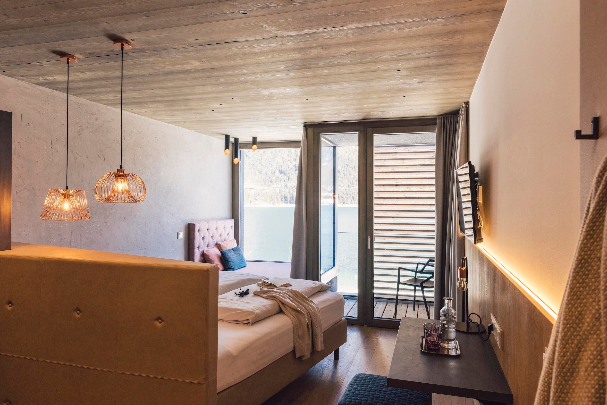 A modern room with a large bed and access to a balcony. The decor is stylish with warm light accents and a pleasant atmosphere.