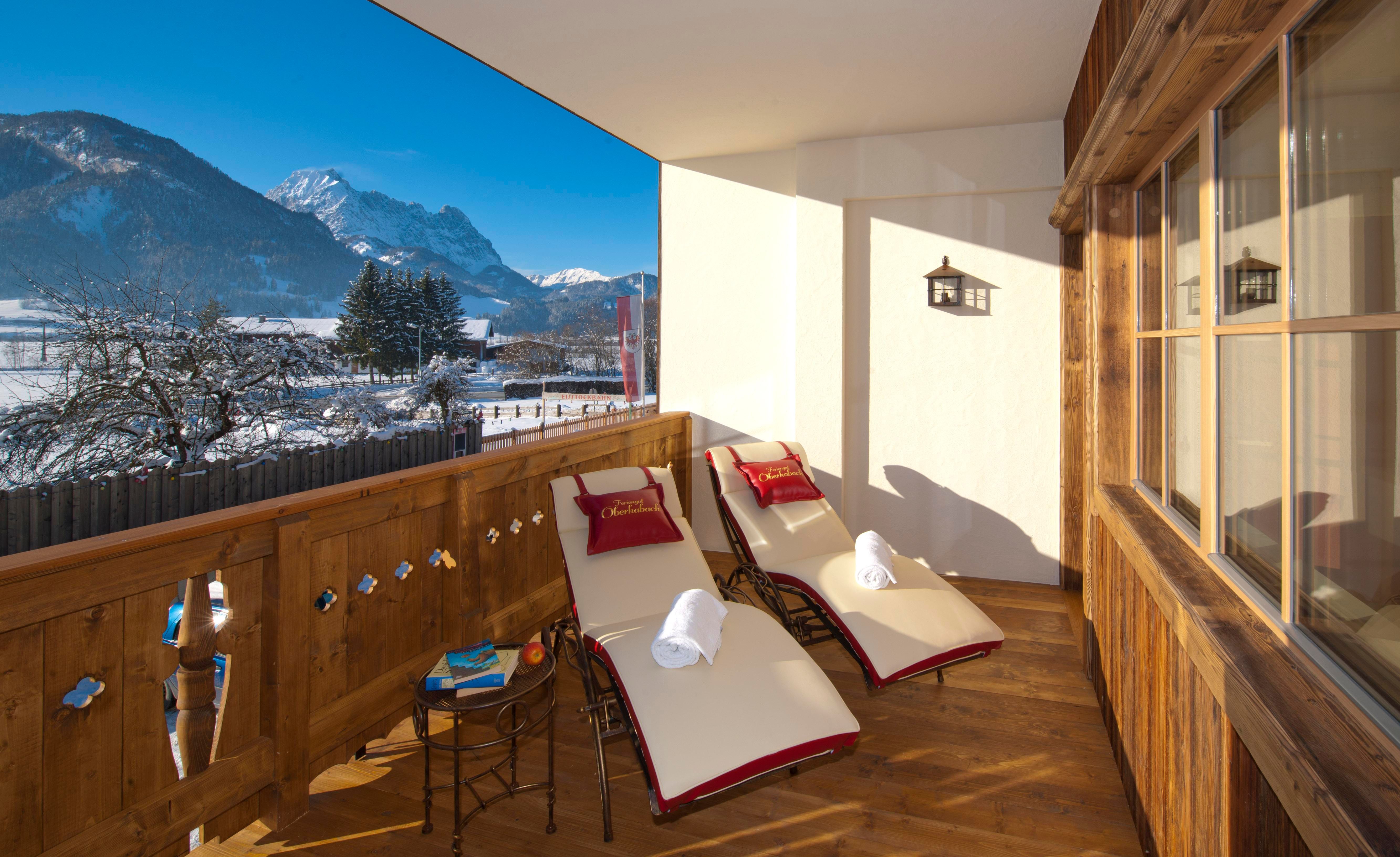 A cozy balcony with two loungers and a small table. In the background, snow-covered mountains and a clear sky can be seen.