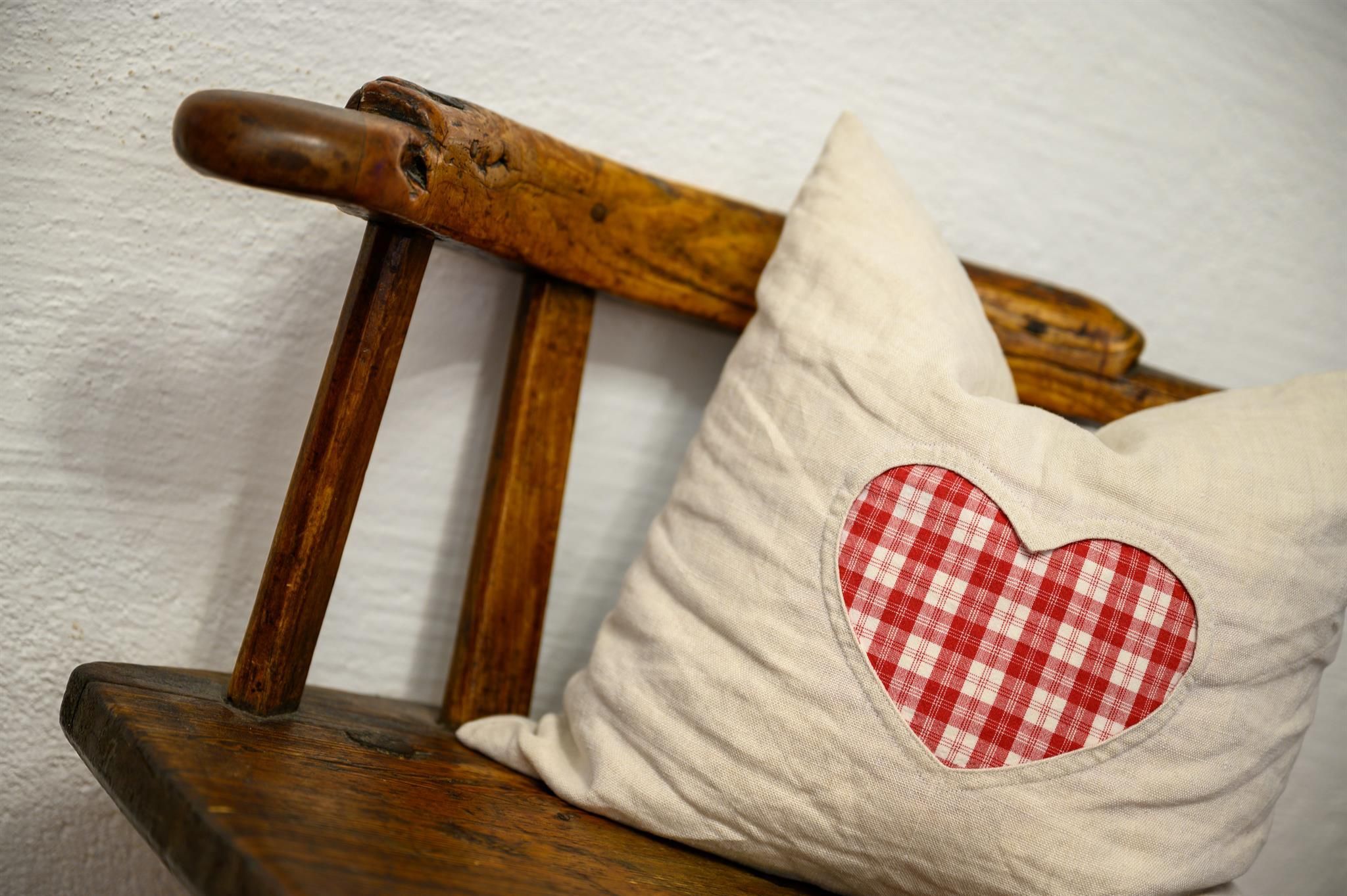 A wooden chair with a cushion that has a red heart pattern. The cushion is placed on the chair and conveys a cozy atmosphere.