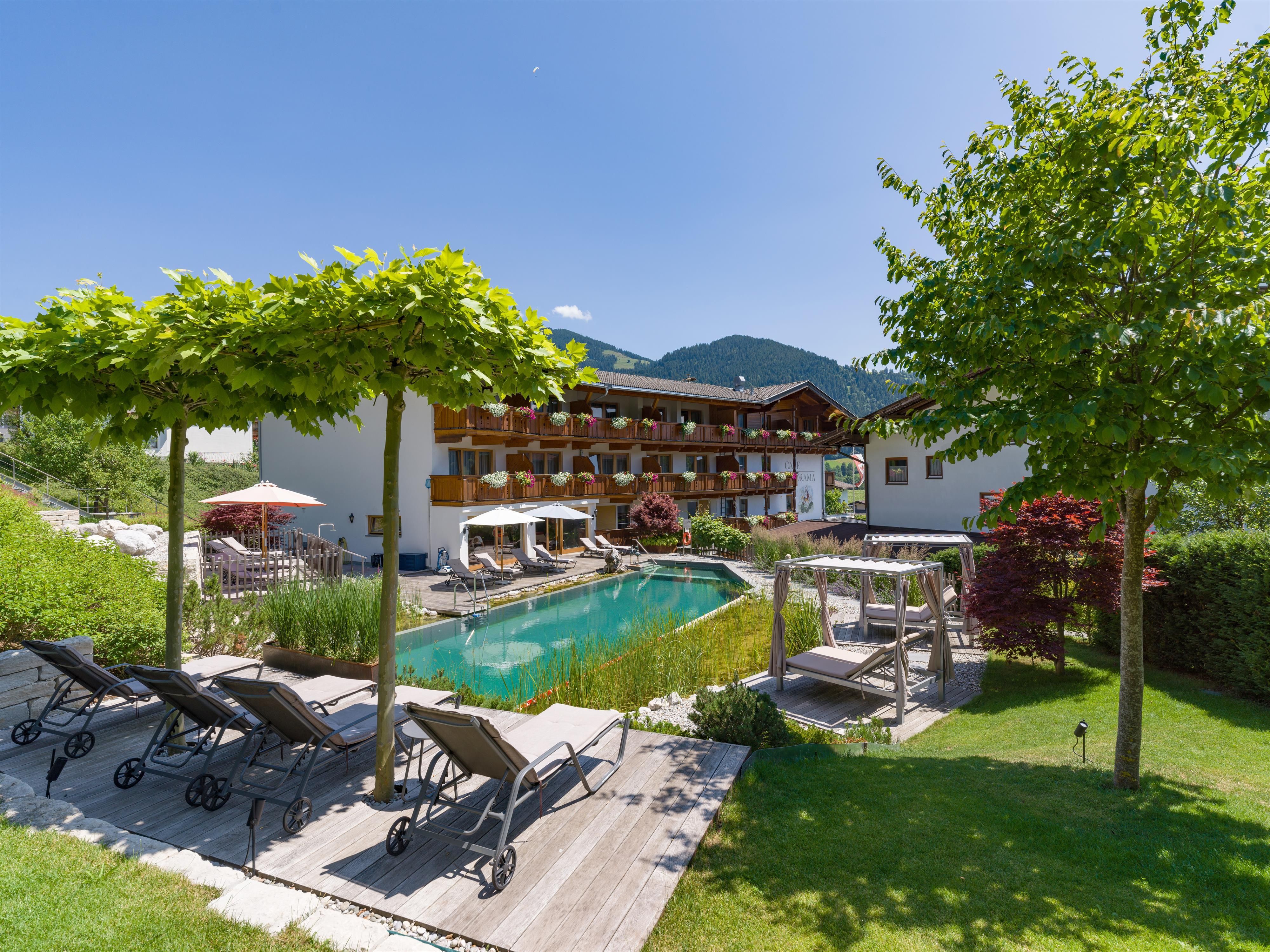 Exterior view of Hotel Alpenpanorama with garden, pool, sun loungers, and view of the Tyrolean mountains.
