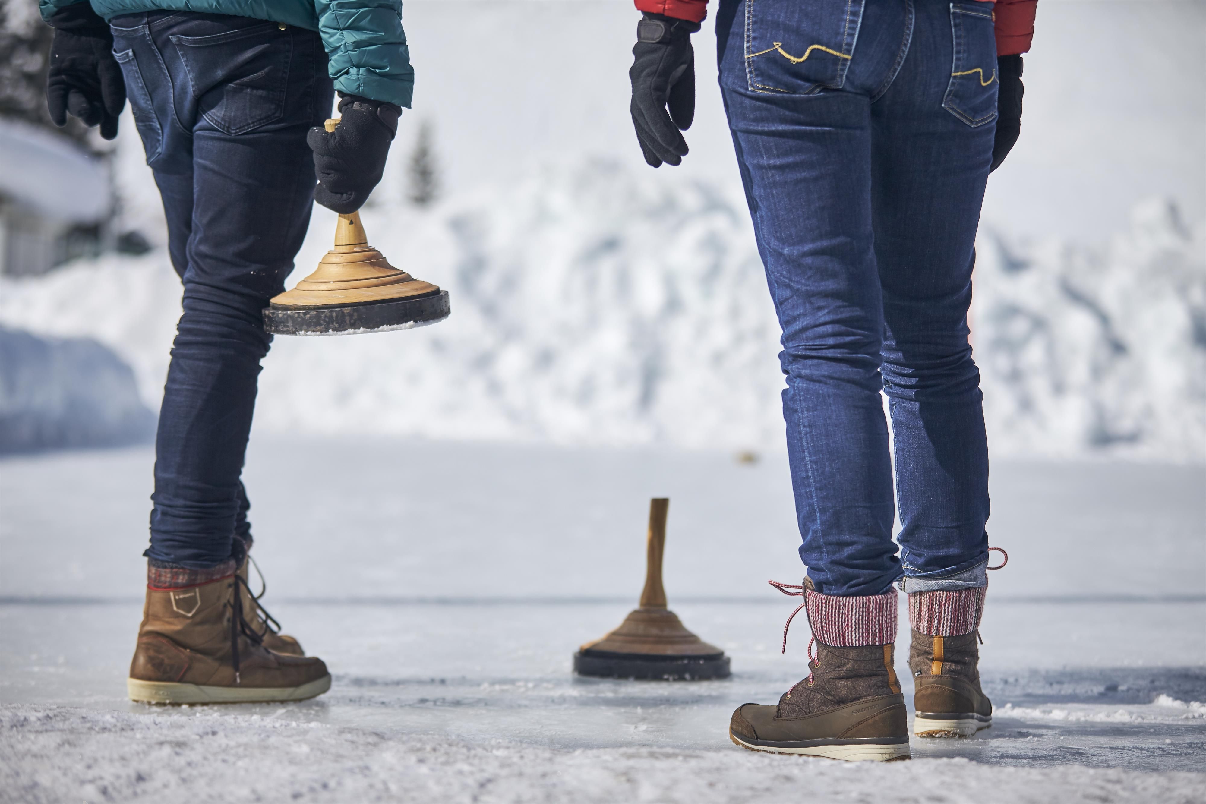 Two people are standing on an icy surface, holding devices in their hands. The background shows snowy landscapes and bright skies.