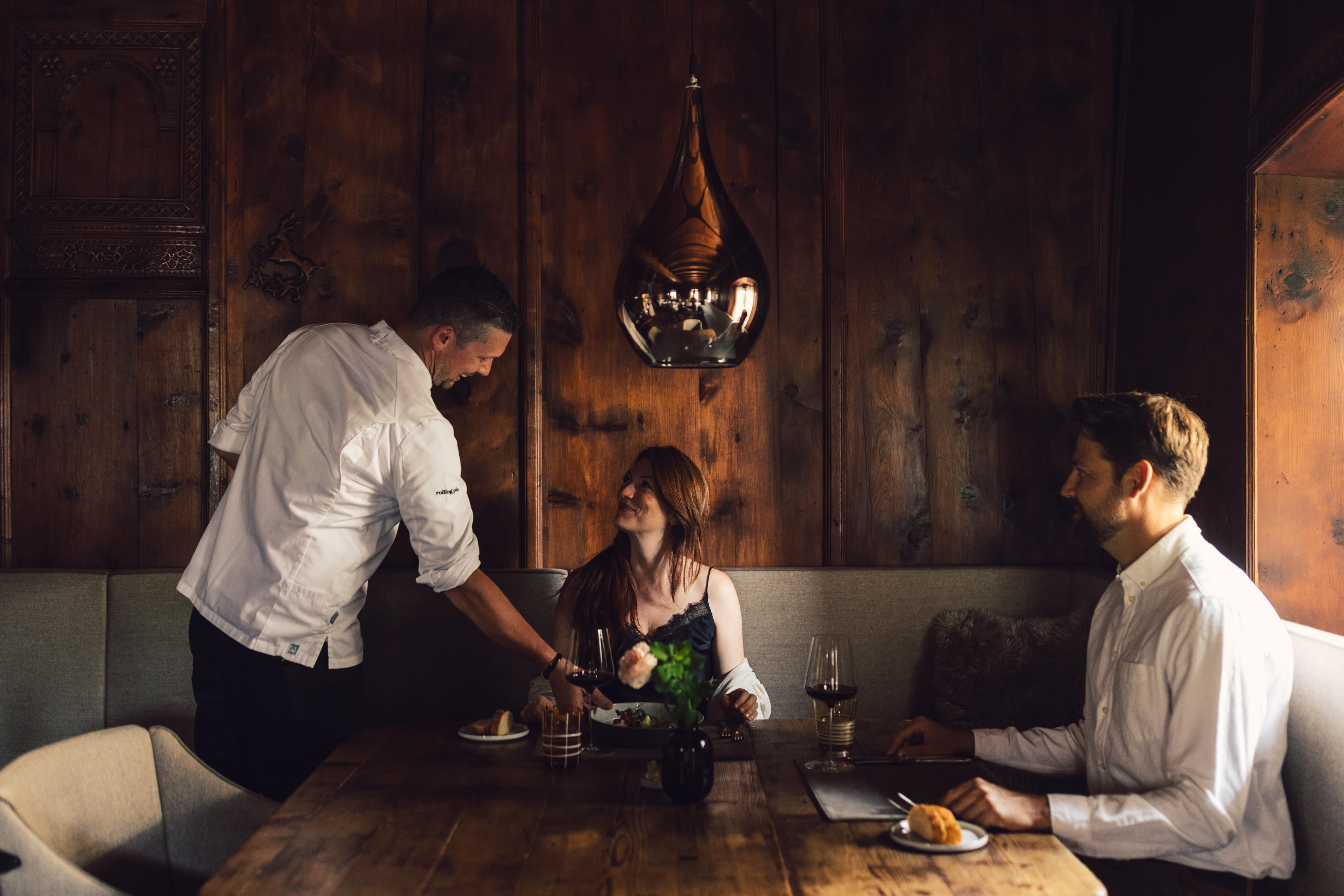 An elegant restaurant with a wooden table. A waiter serves a dish at a table where a couple is sitting.