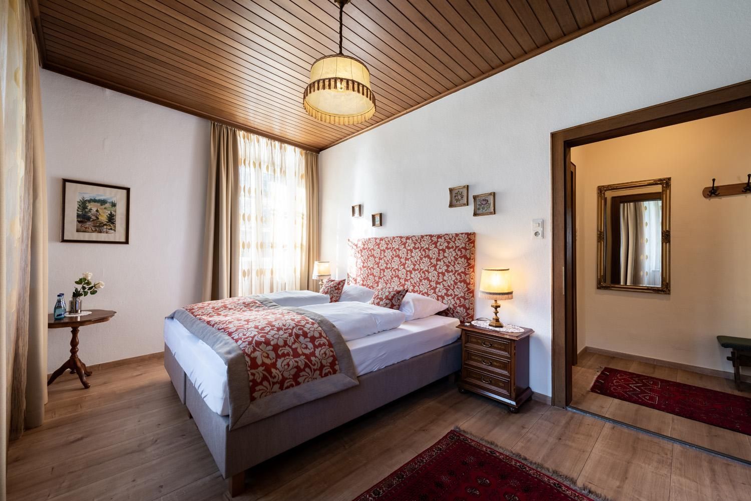 A cozy bedroom with a large bed and a bright wooden ceiling. The decor is stylish with floral patterns and warm colors.