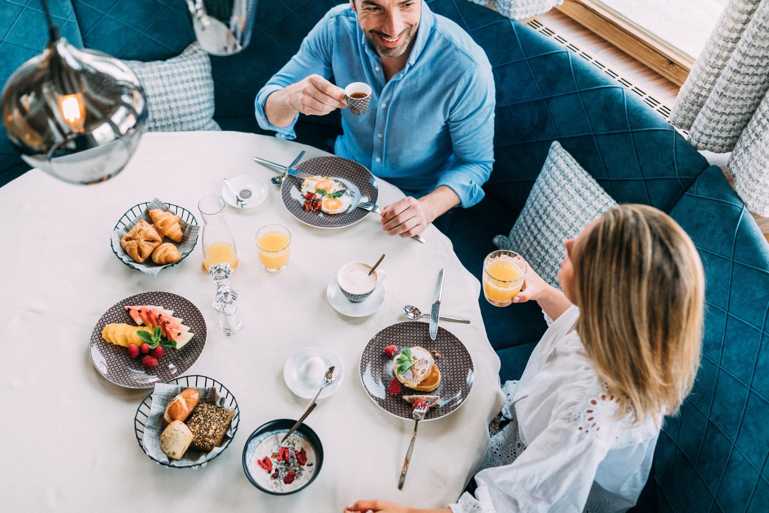 A breakfast table with various foods and drinks. Two people are enjoying the meal in a cozy atmosphere.