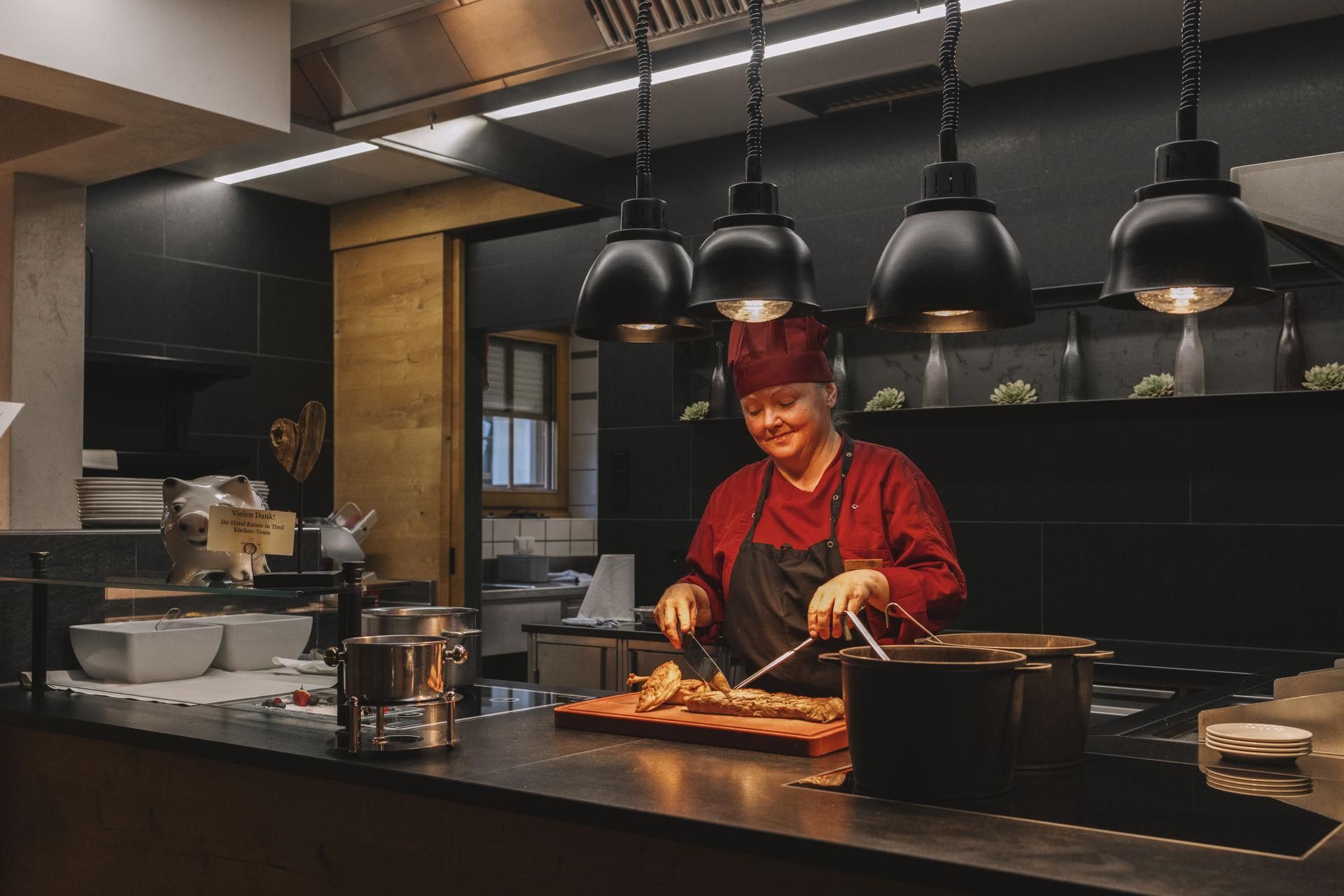 A cook in a modern kitchen is preparing dishes. He is wearing a red chef's hat and smiling while he works at a table.