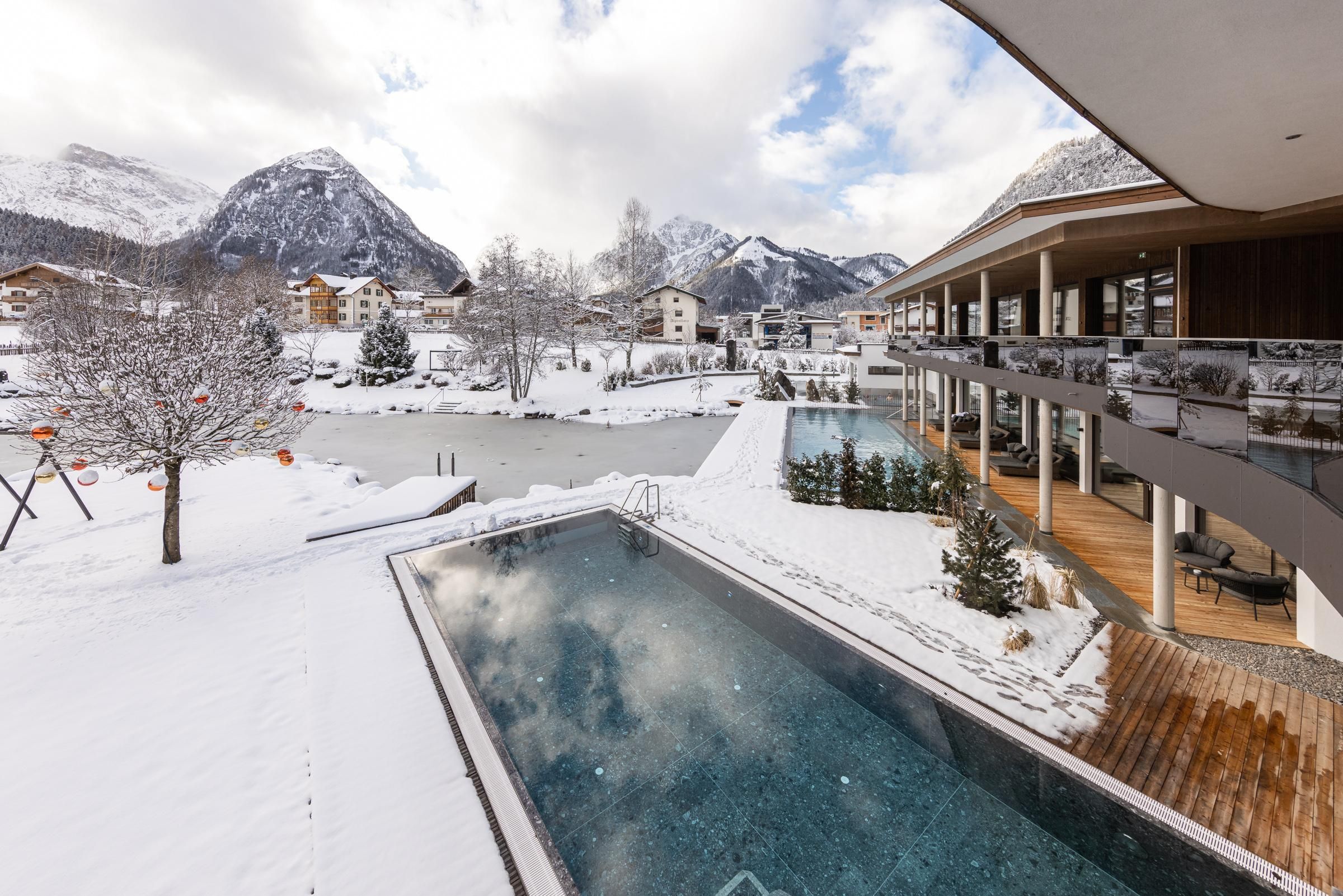 A modern living area with an outdoor pool in a snowy landscape. In the background, mountains and a calm lake can be seen.