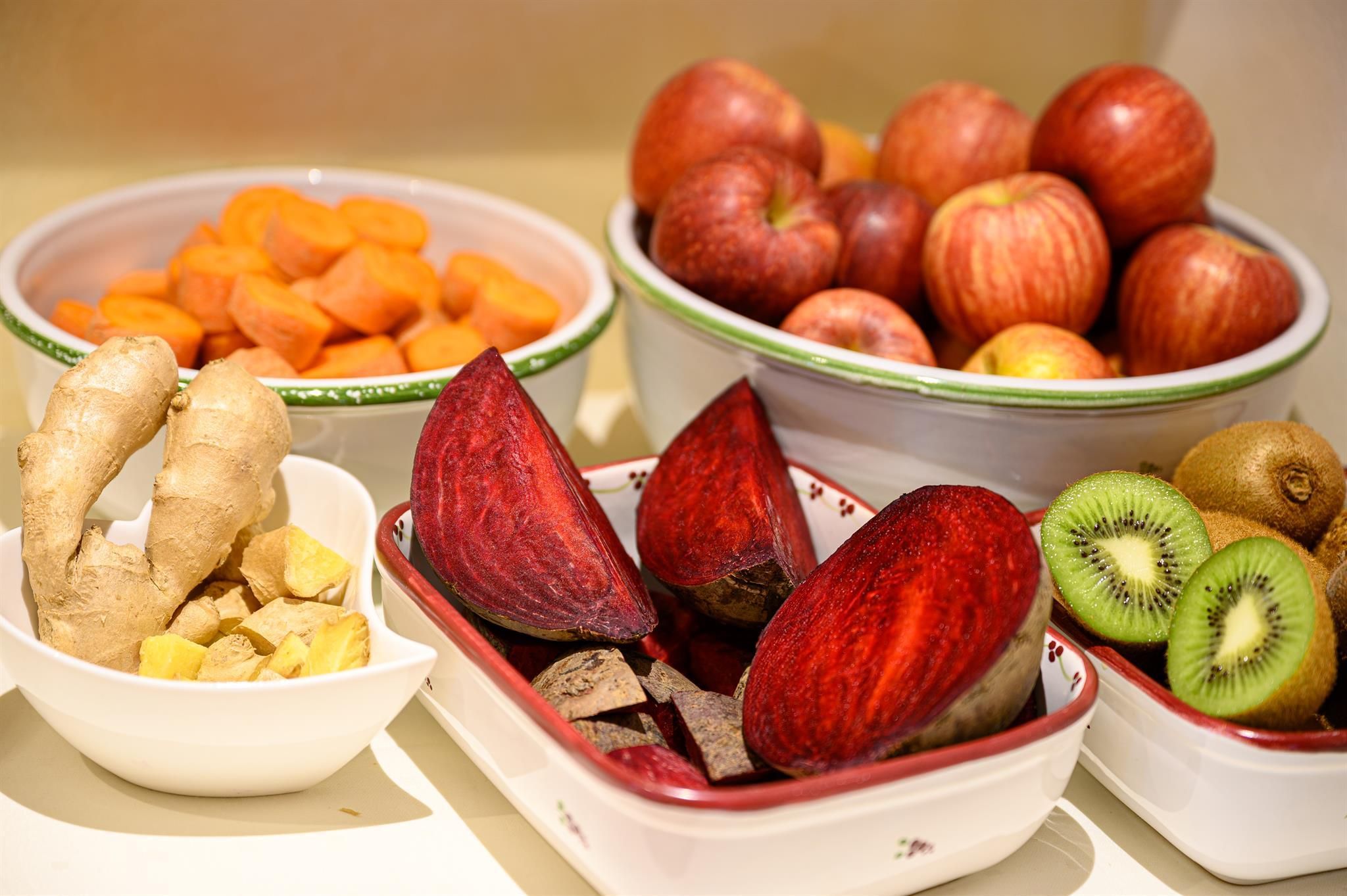 A selection of fresh fruits and vegetables, including apples, kiwis, carrots, and beets. In the foreground, there are also pieces of ginger.