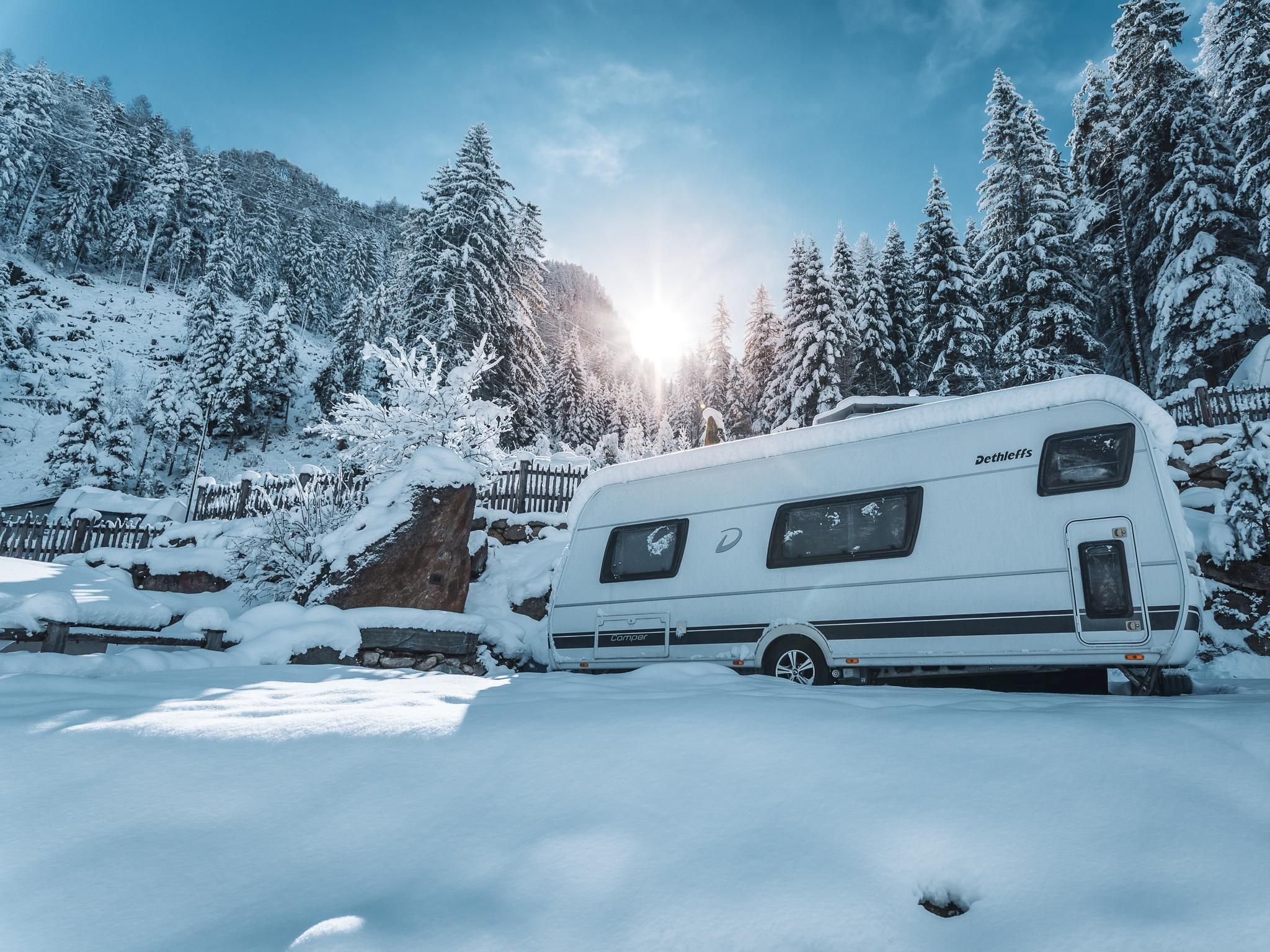 A motorhome is standing in a snow-covered landscape. In the background, there are snow-covered trees and a sunny sky.