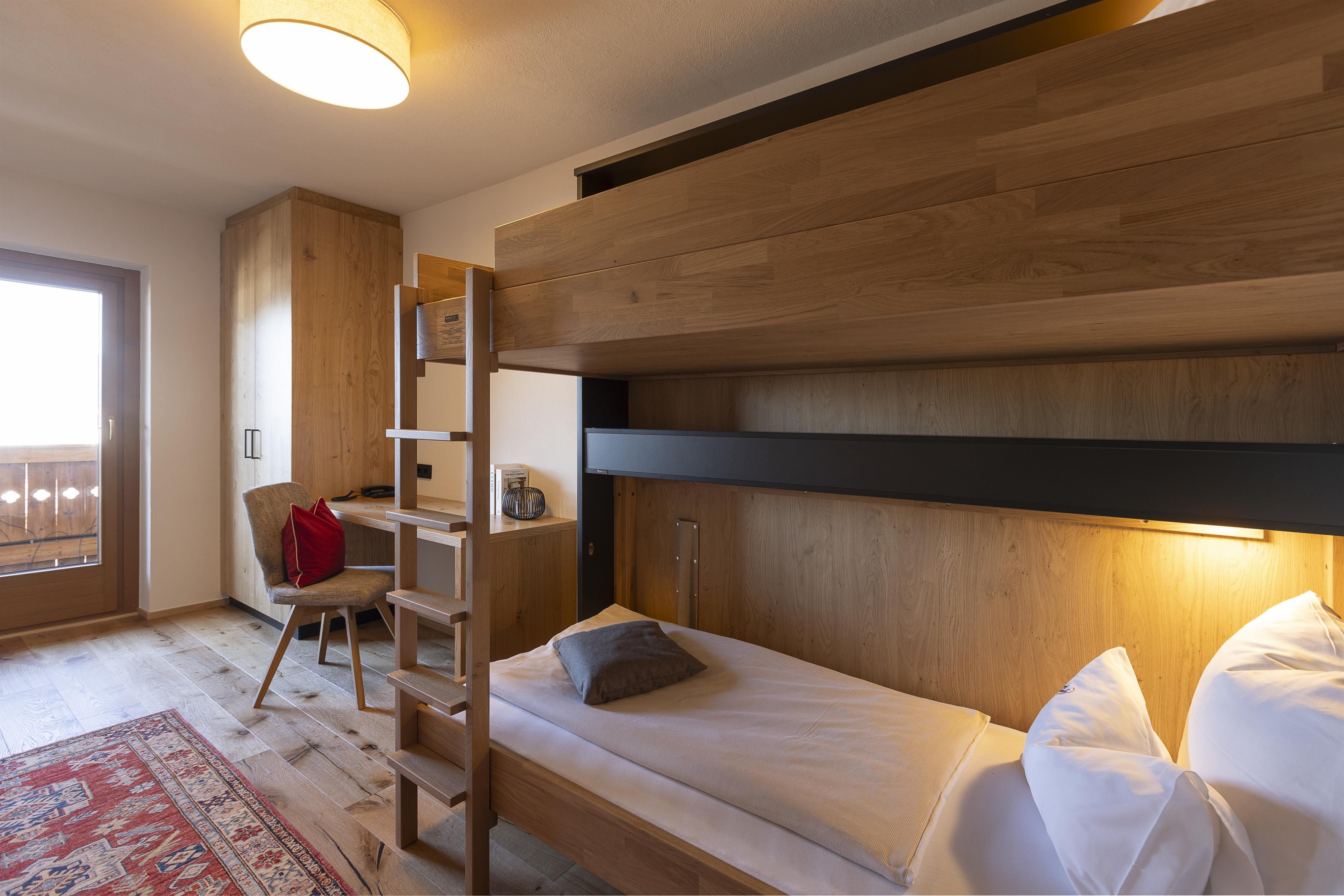 A modern room with wooden interior and a loft bed. There is a desk and a balcony with a view outside.