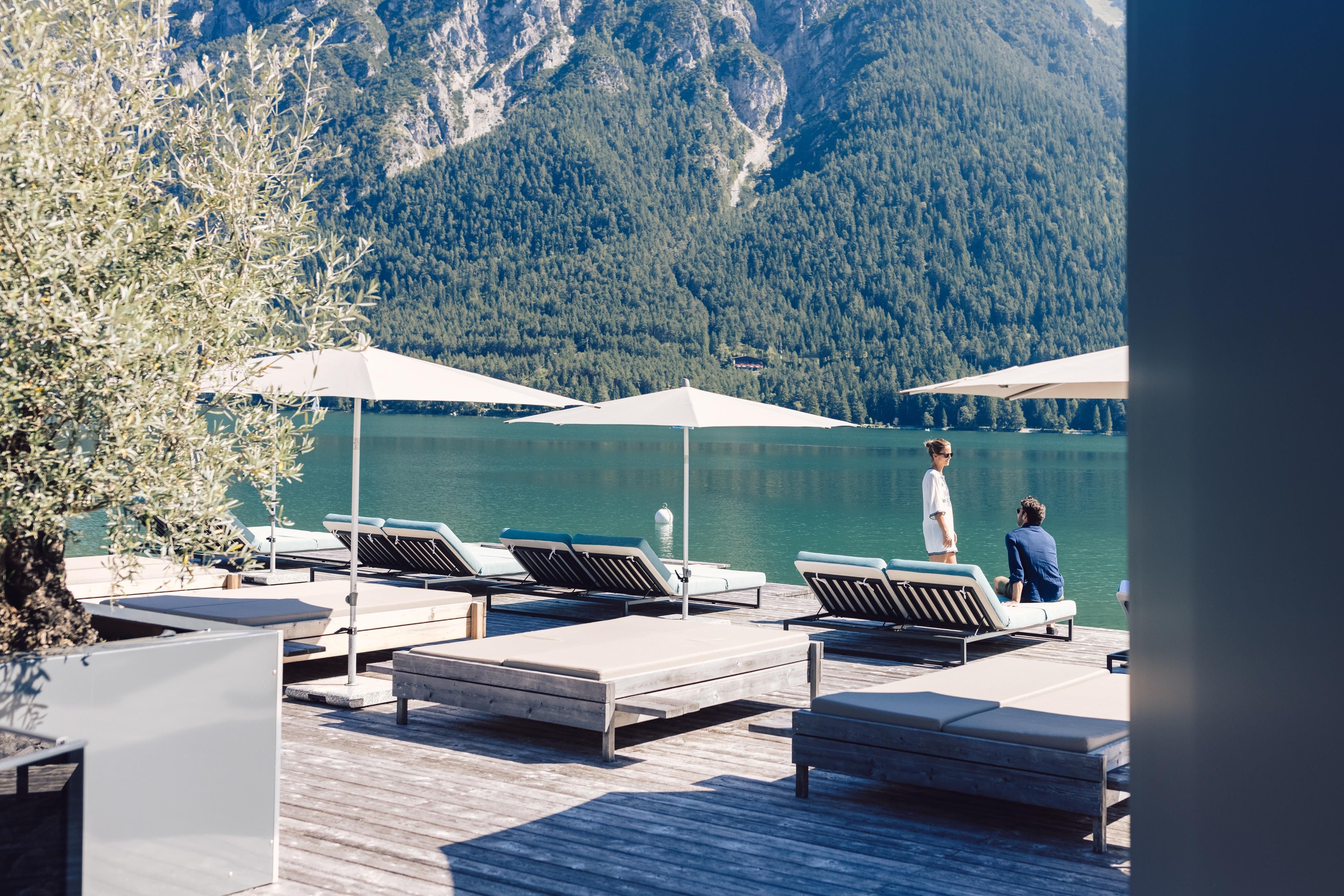 A peaceful lake with sun loungers and beach umbrellas. Impressive mountains can be seen in the background.