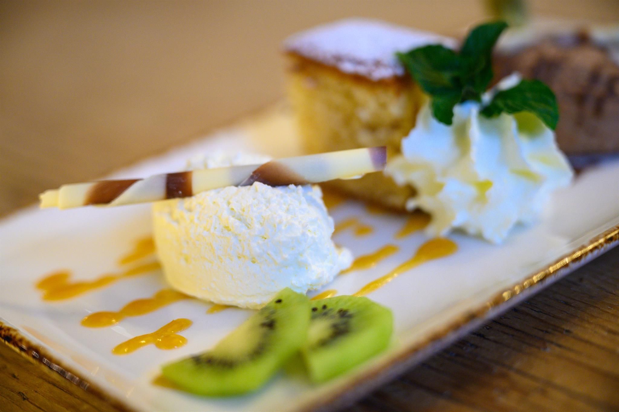 A delicious dessert on a plate with whipped cream, ice cream, and a piece of cake. Fresh kiwi and a chocolate decoration complete the whole.