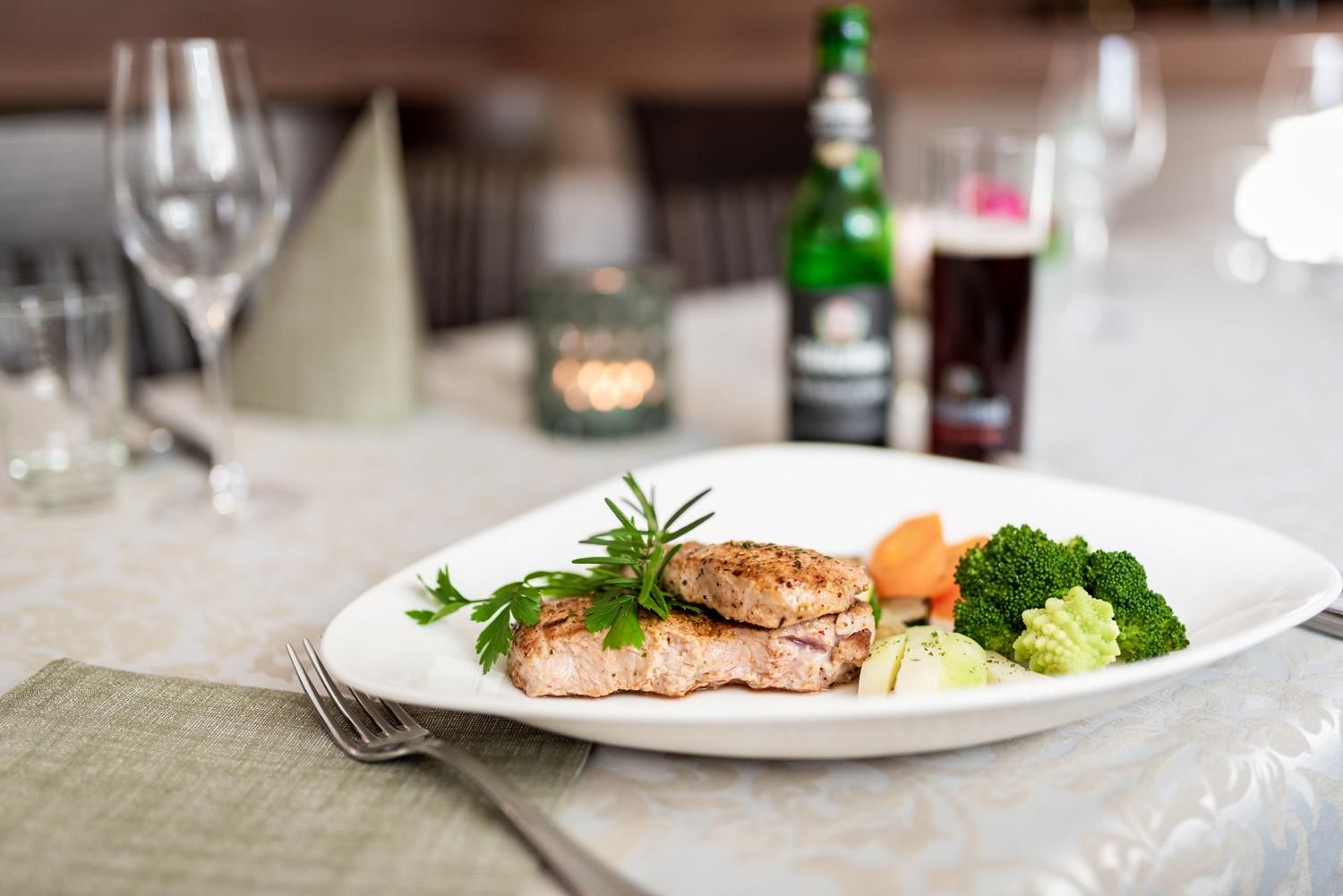 An appealingly arranged plate with fried fish and vegetables. In the background, glasses and drinks are visible.