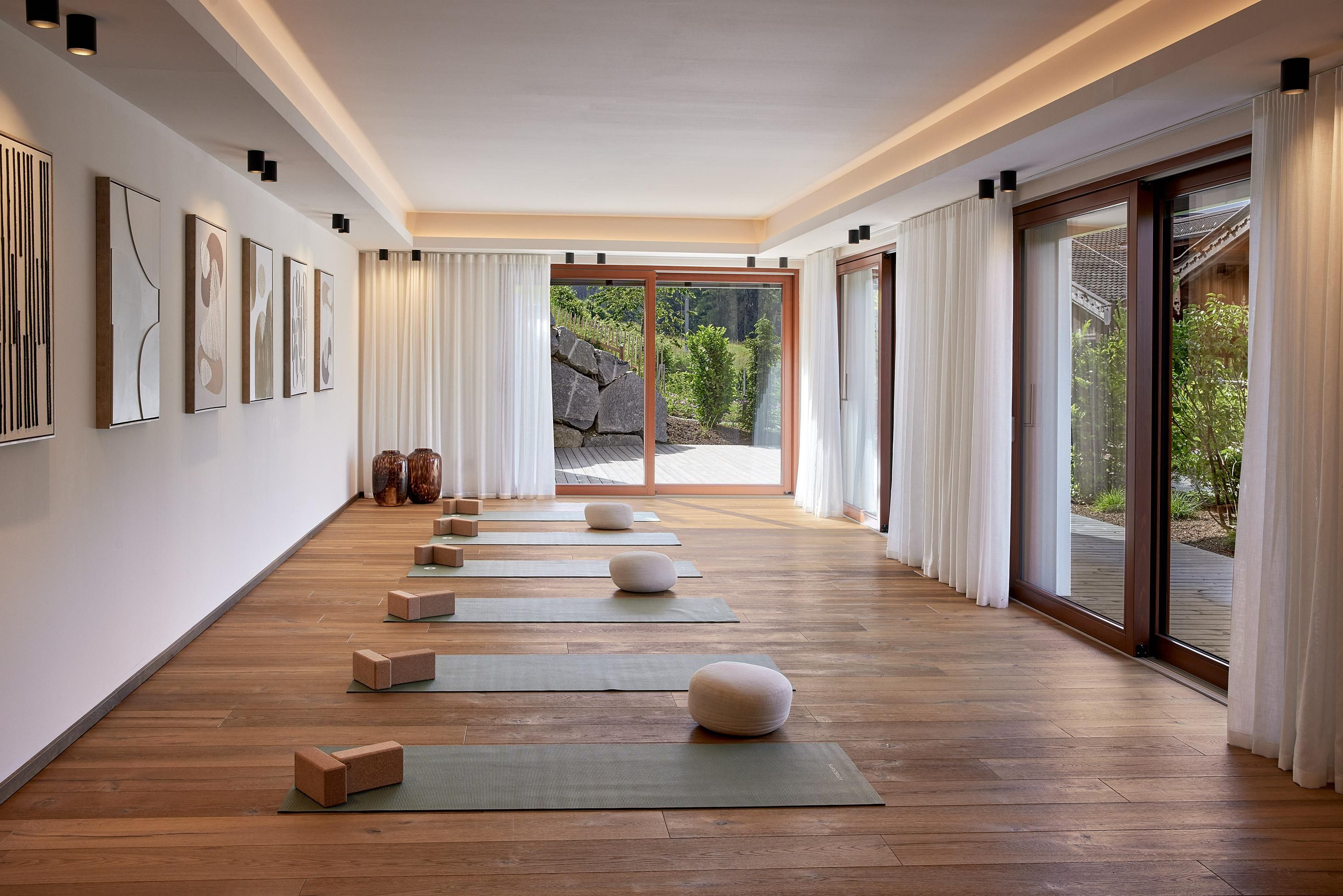 A bright and quiet yoga room with mats and cushions. Large windows allow for plenty of daylight and a view of the greenery.