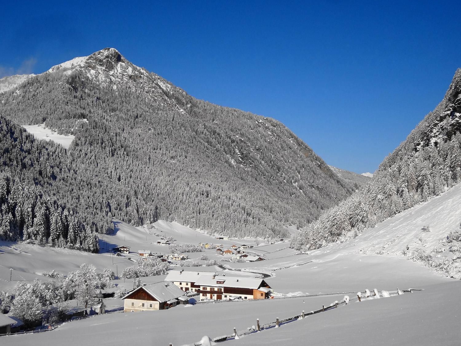 A winter landscape with snow-covered mountains and a small village in the valley. The clear blue sky makes the scene look fresh and inviting.