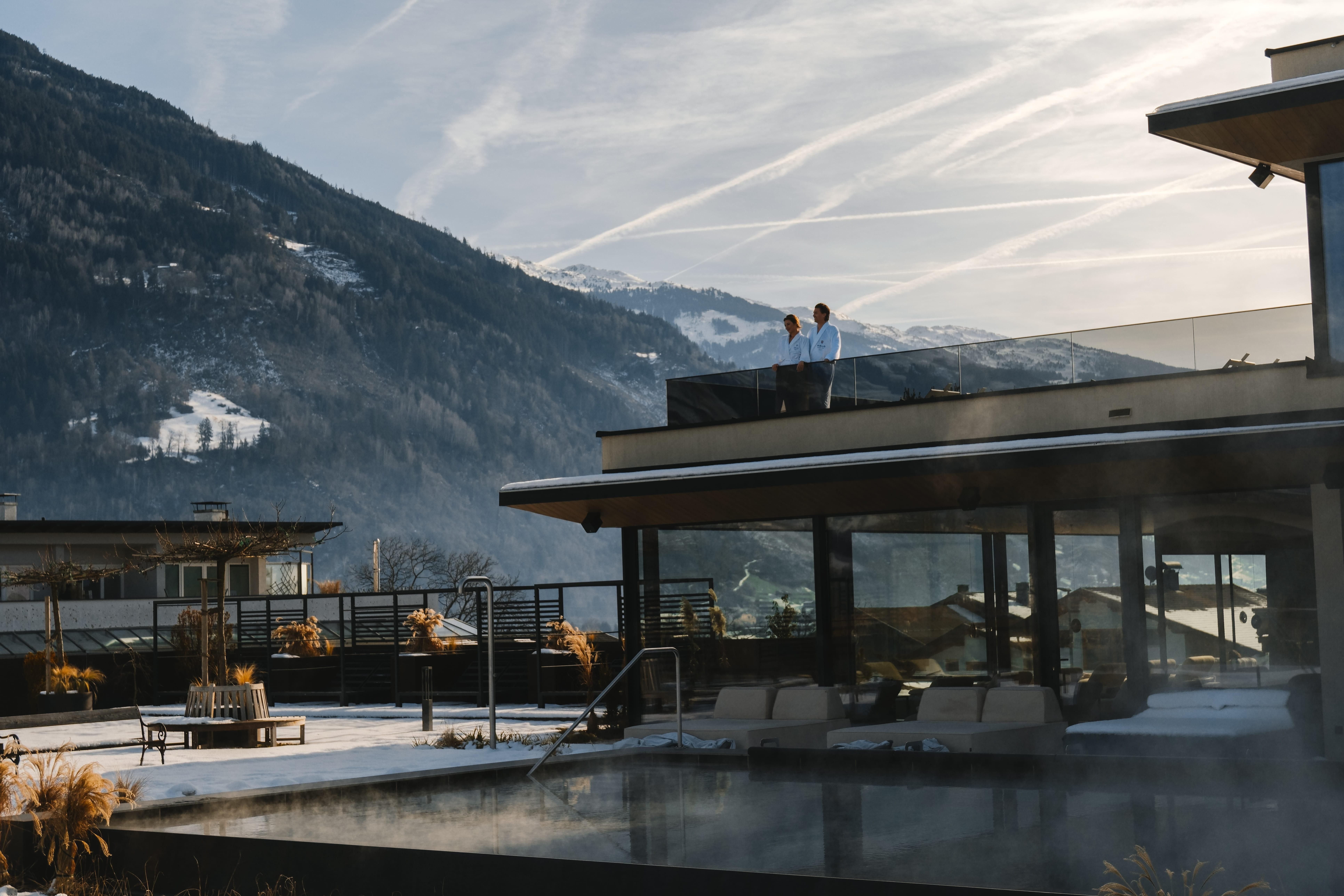 A modern terrace with a view of a majestic mountain landscape. Two people are standing relaxed and enjoying the view.