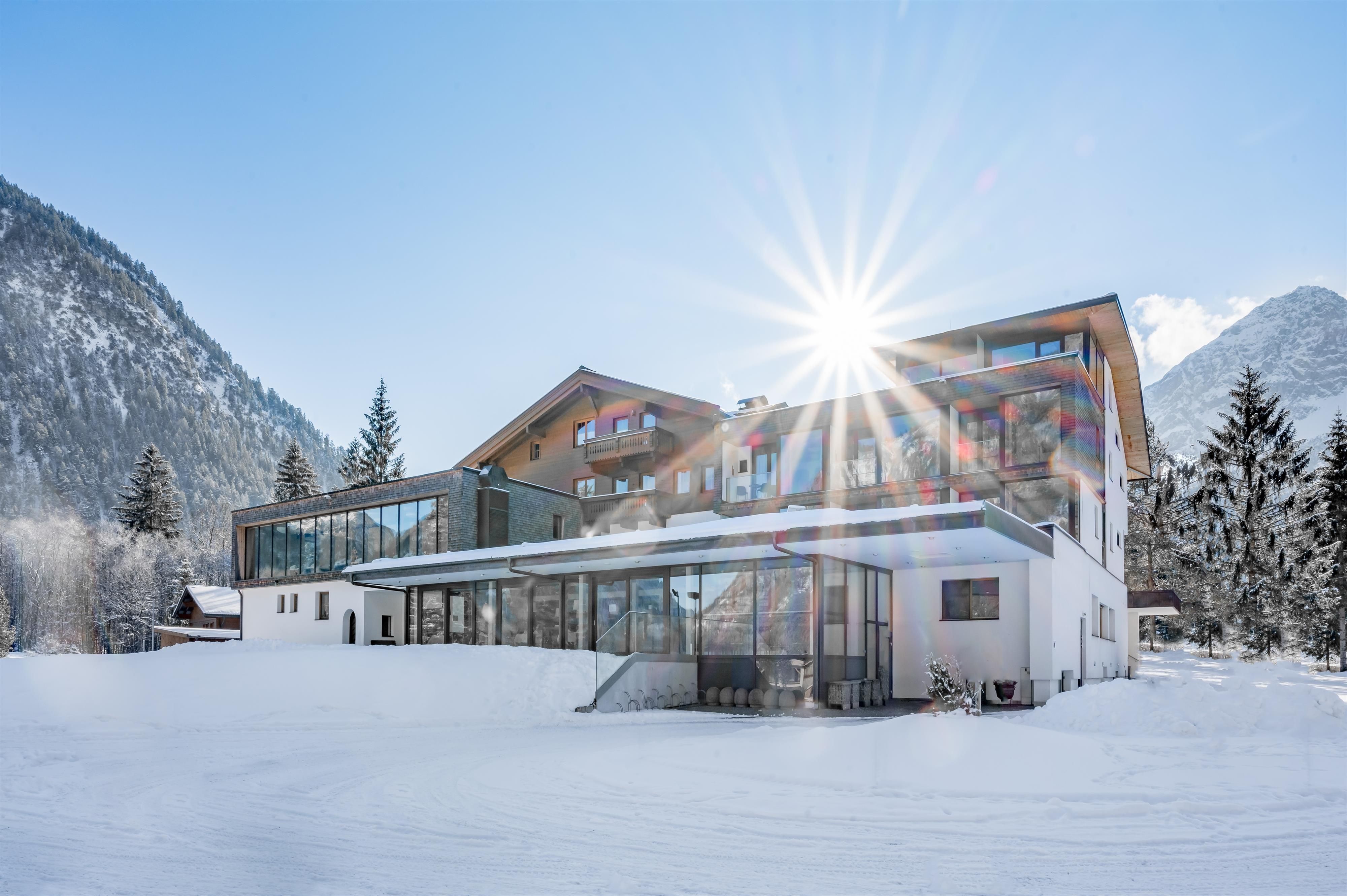 A modern building in the snow with a stunning mountain backdrop. The sun shines brightly, giving the scene a warm atmosphere.