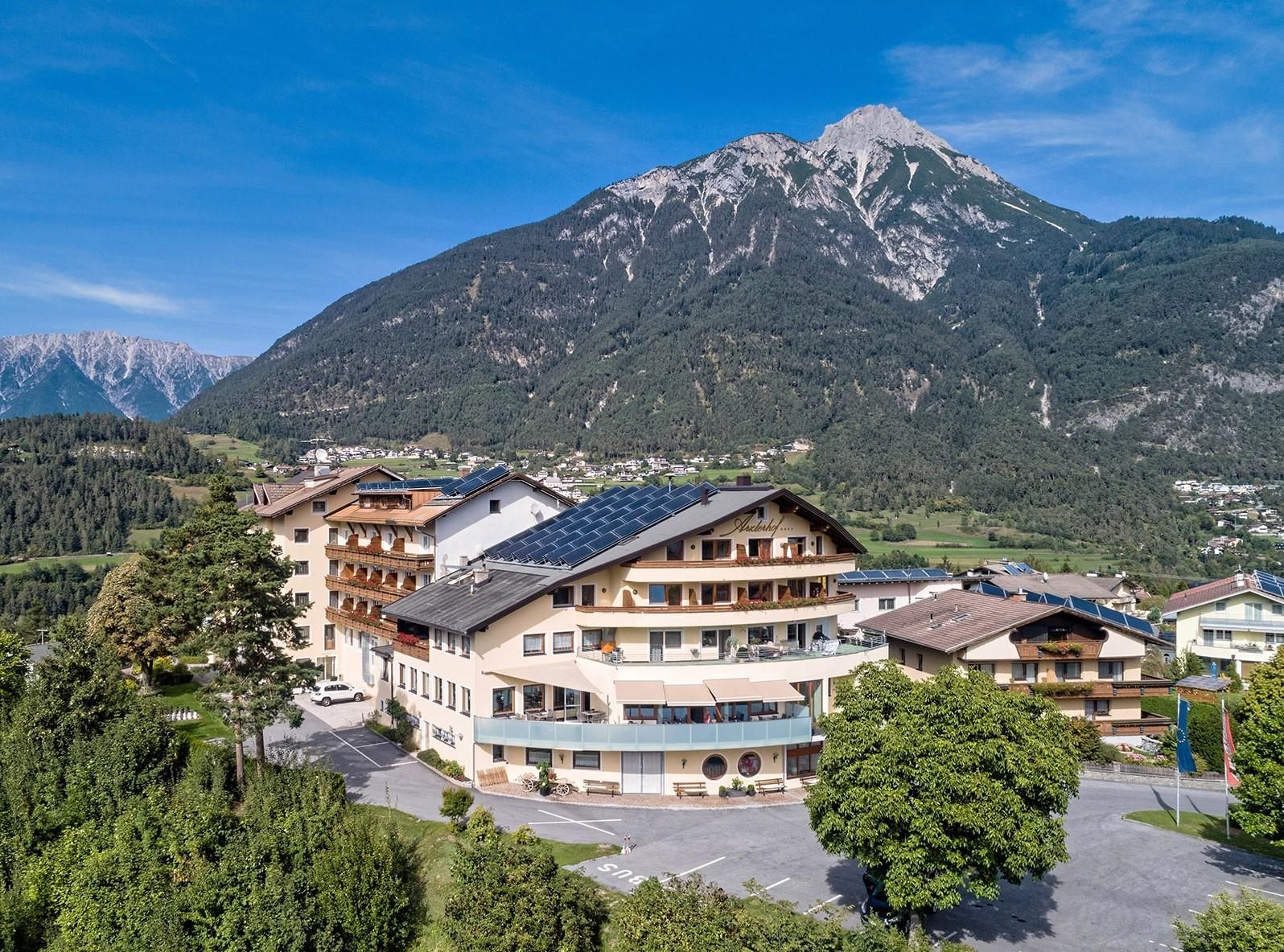 A charming hotel with modern amenities, surrounded by green forests and stunning mountains. The clear sky provides a picturesque view of nature.