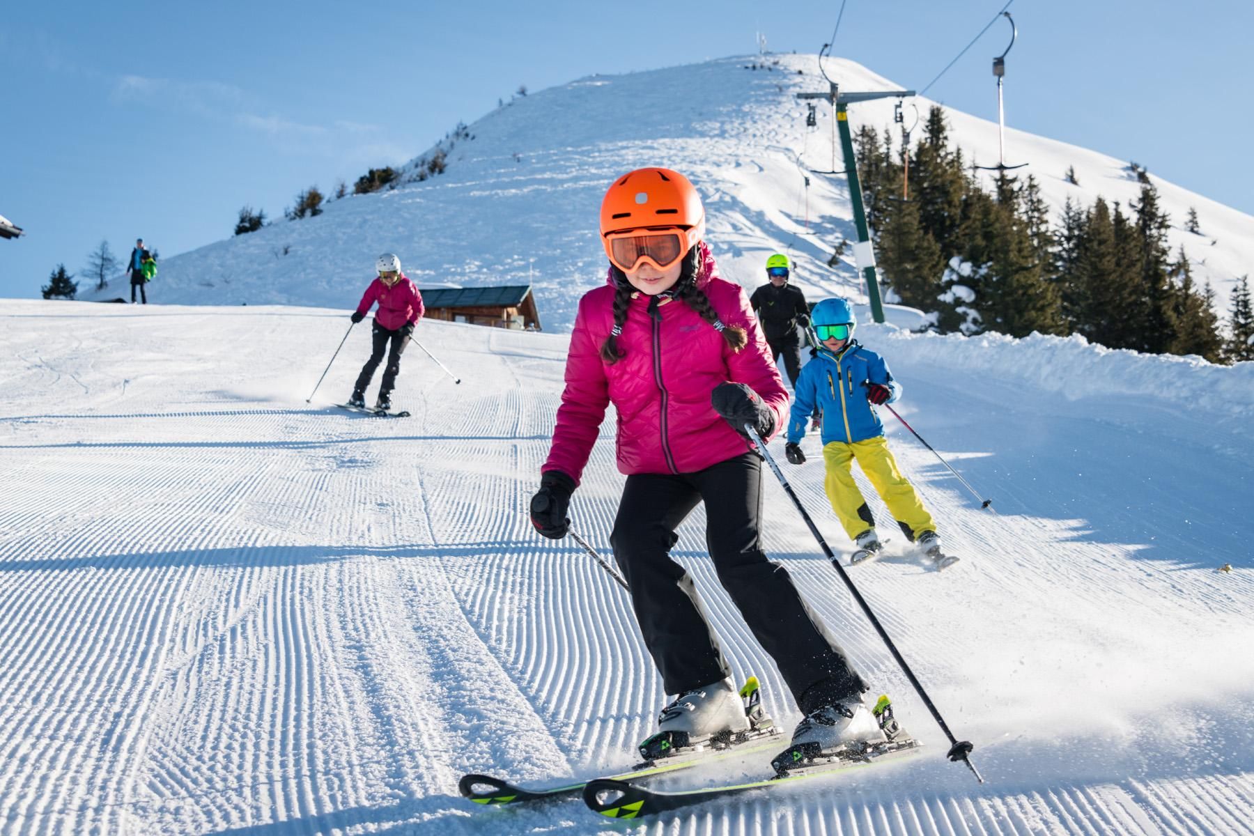 A ski resort with several skiers on the slope. The sun is shining on the snow-covered hillside.