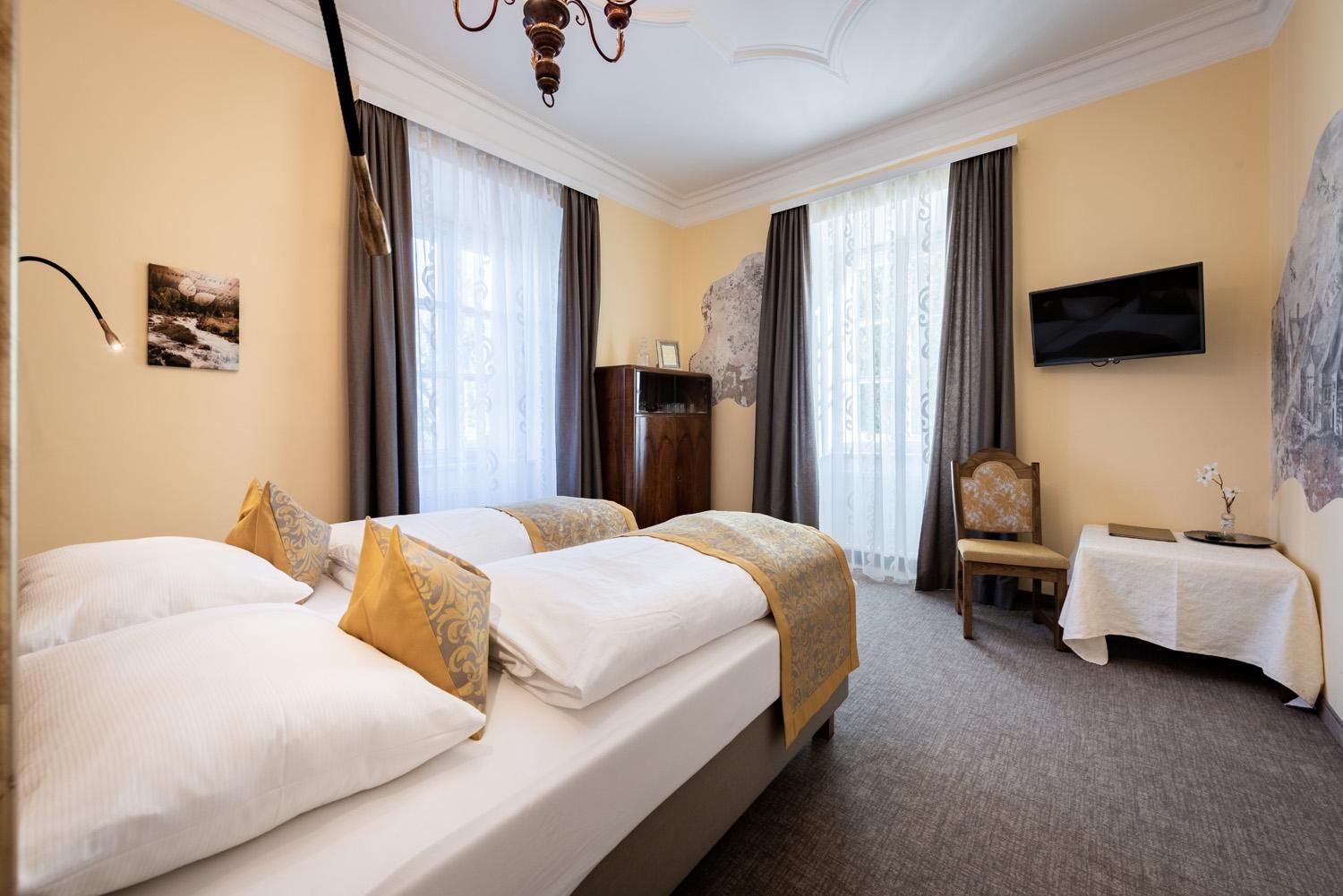 A cozy room with two beds and a bright, friendly ambiance. Large windows provide plenty of daylight and a pleasant atmosphere.