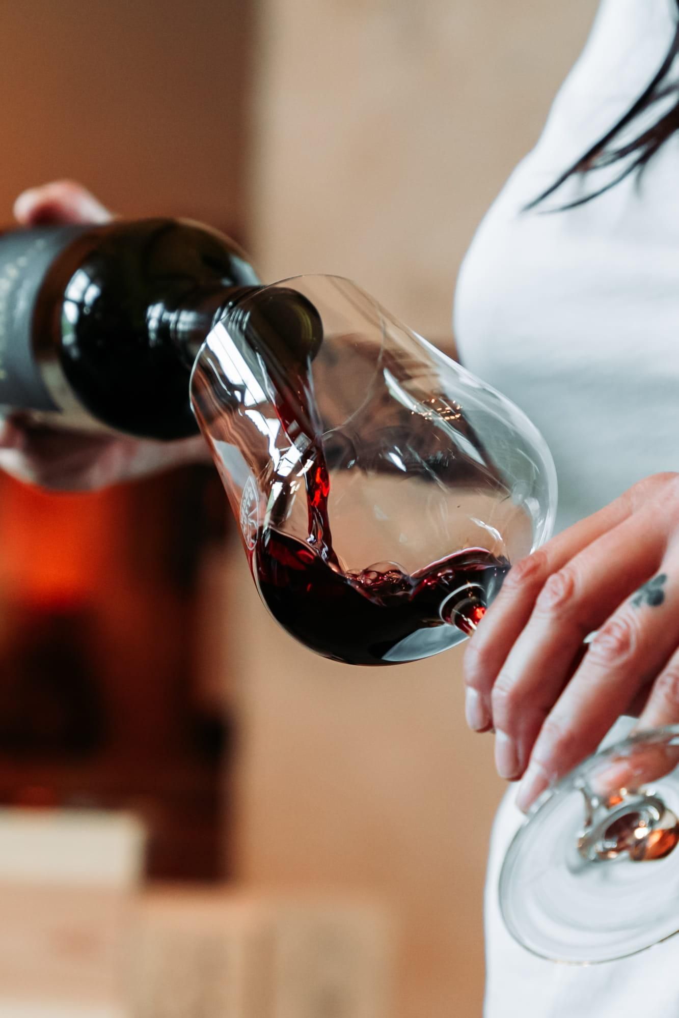 A glass of red wine is poured from a bottle. The hand holds the glass elegantly as the wine flows into the glass chalice.