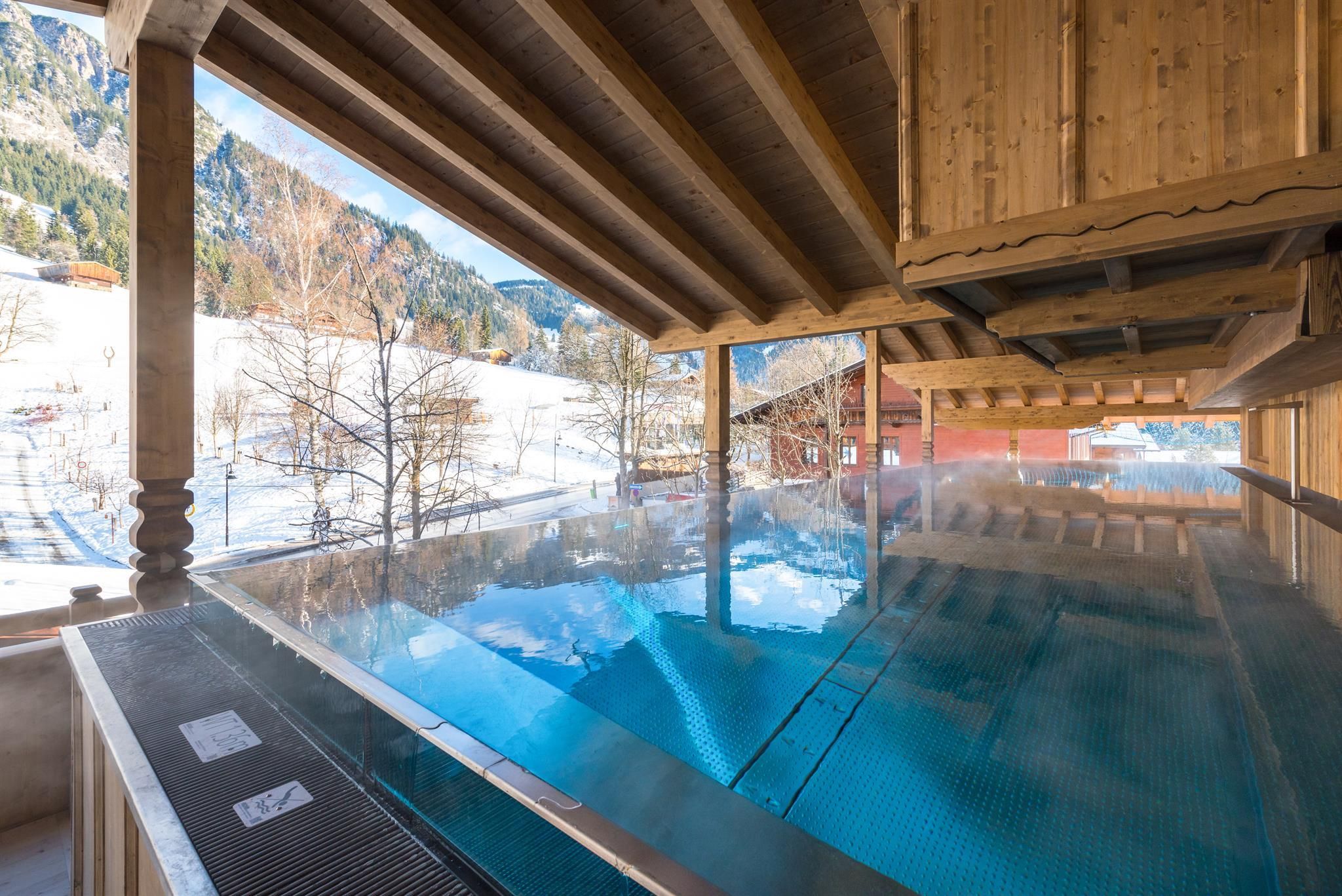 A stylish indoor pool with wooden construction and a view of the snow-covered landscape. Quiet and relaxing atmosphere in winter.