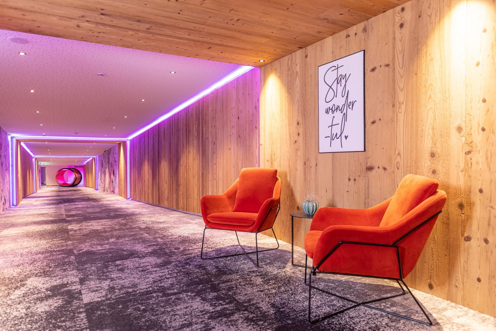 A modern hallway with wooden paneling and colorful lights. Two red armchairs are decoratively placed next to each other.