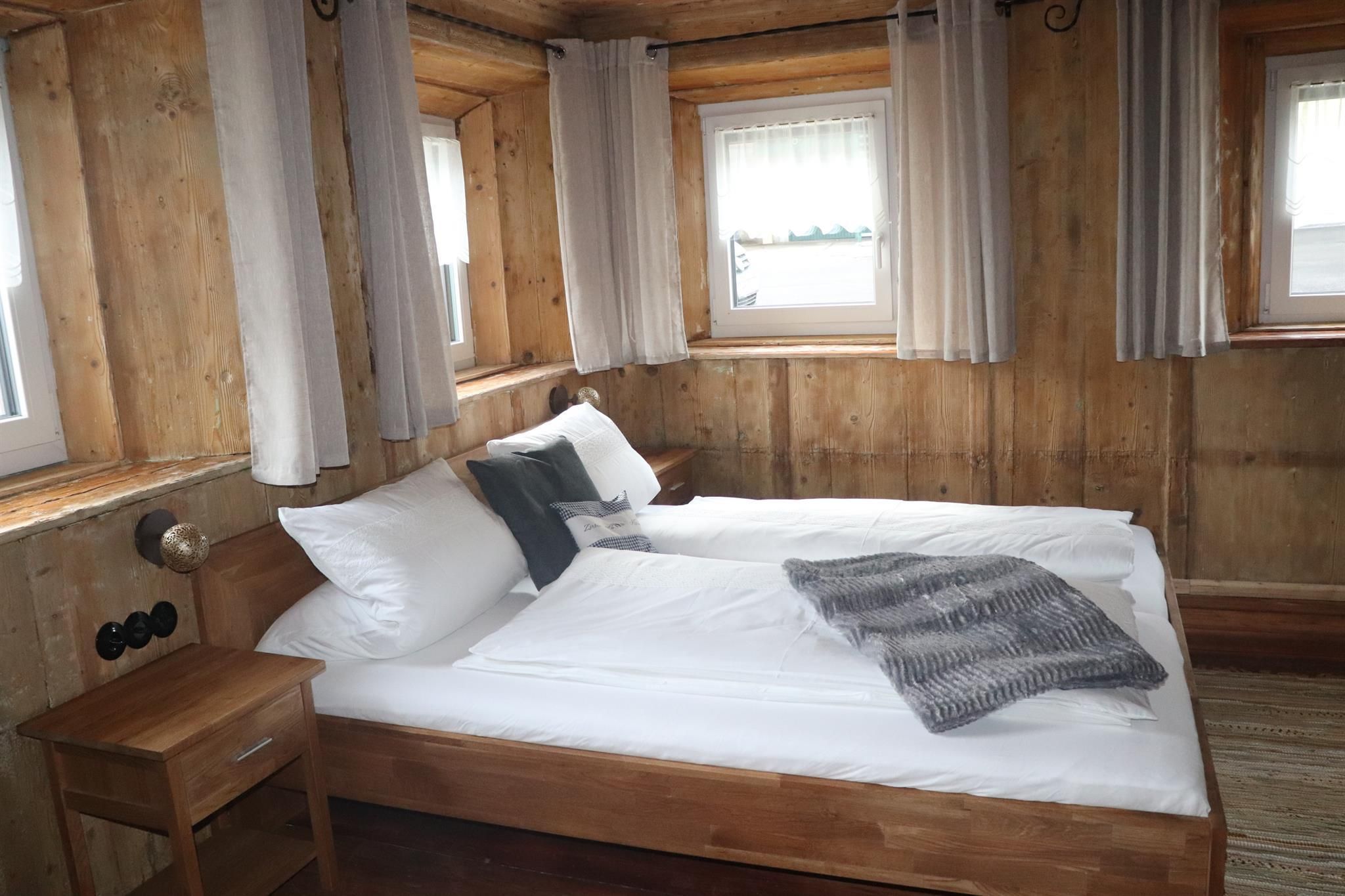 A cozy bedroom with a double bed and wood paneling. The large windows let in plenty of light.