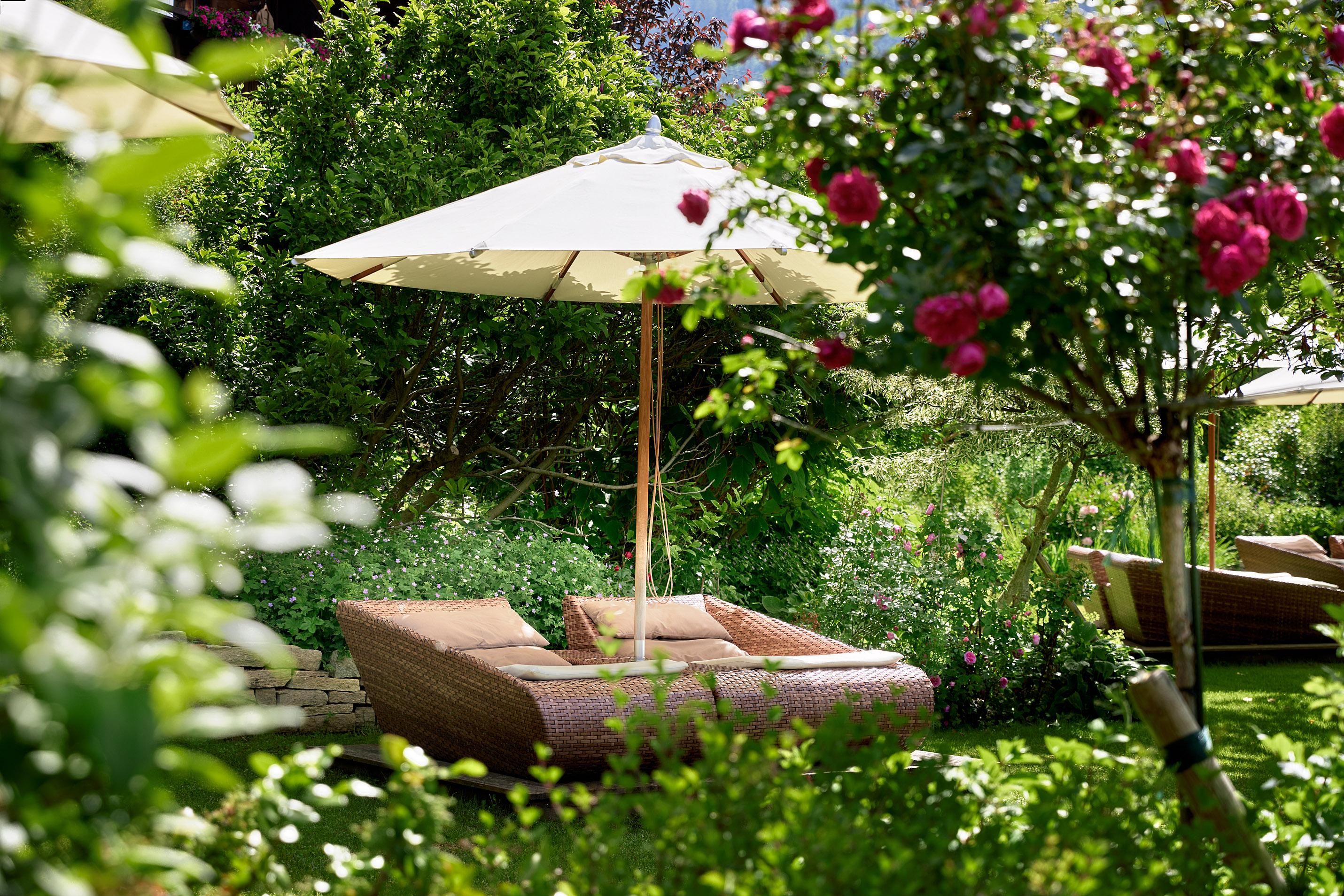 A beautiful garden with loungers and a sun umbrella.
Surrounded by green plants and blooming roses.