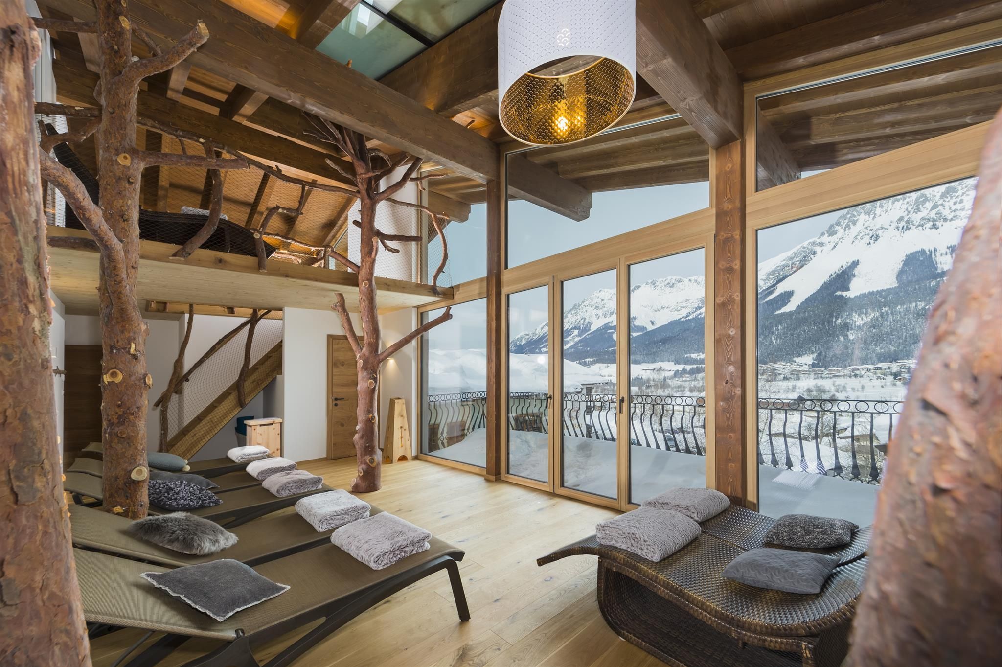 A modern, bright living room with wood decor, large windows, and a view of the mountains. There are loungers and a cozy atmosphere.