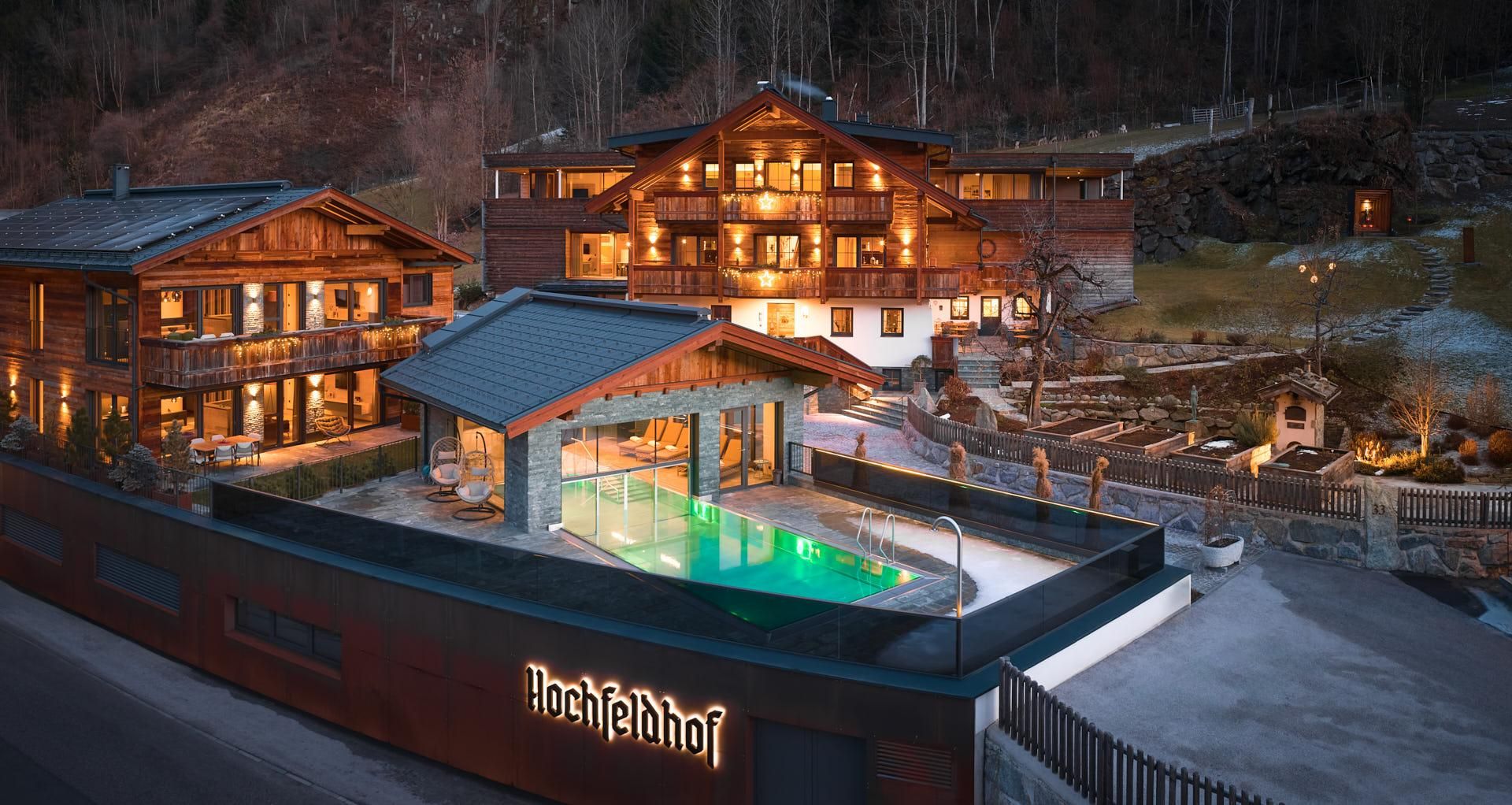 A modern hotel building with a wooden facade and illuminated outdoor area. In the foreground, there is a pool filled with green water.