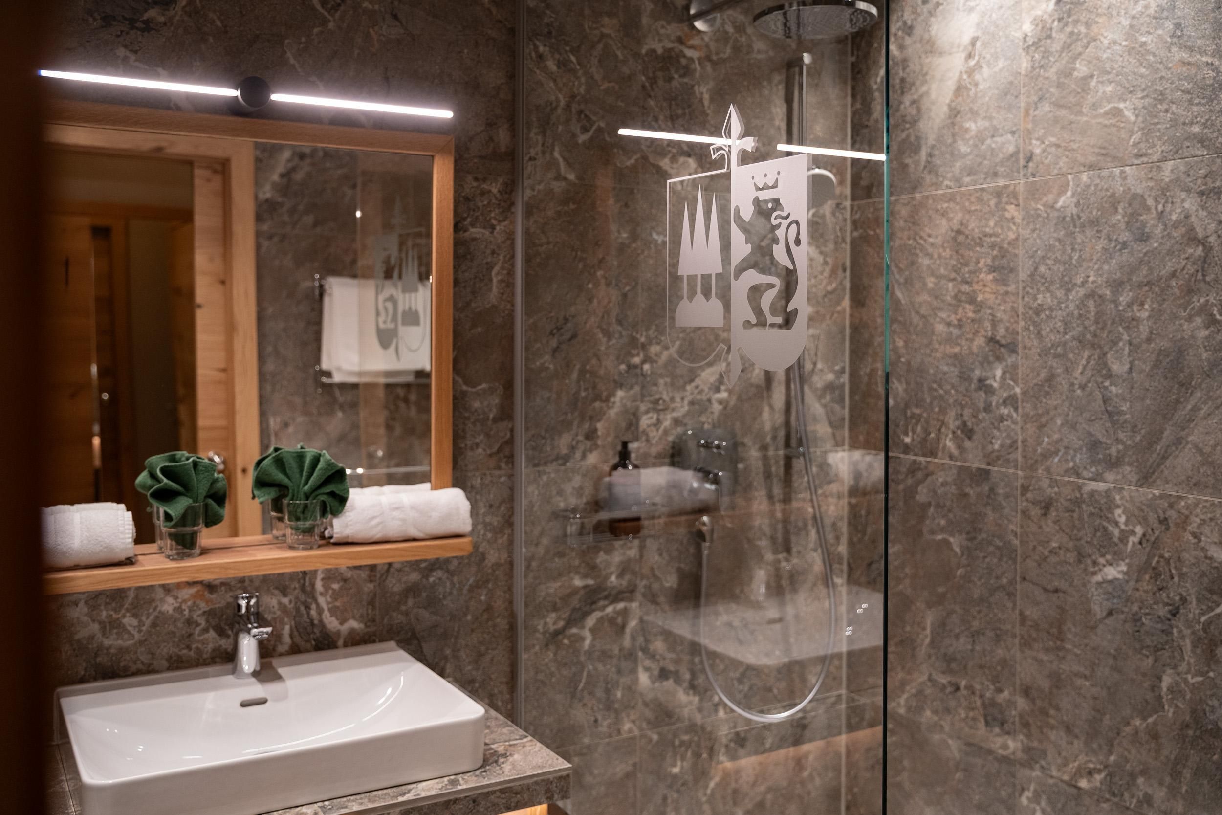 A modern bathroom with elegant marble walls and a walk-in shower. Neatly arranged towels and decorative plants are placed on the dresser.
