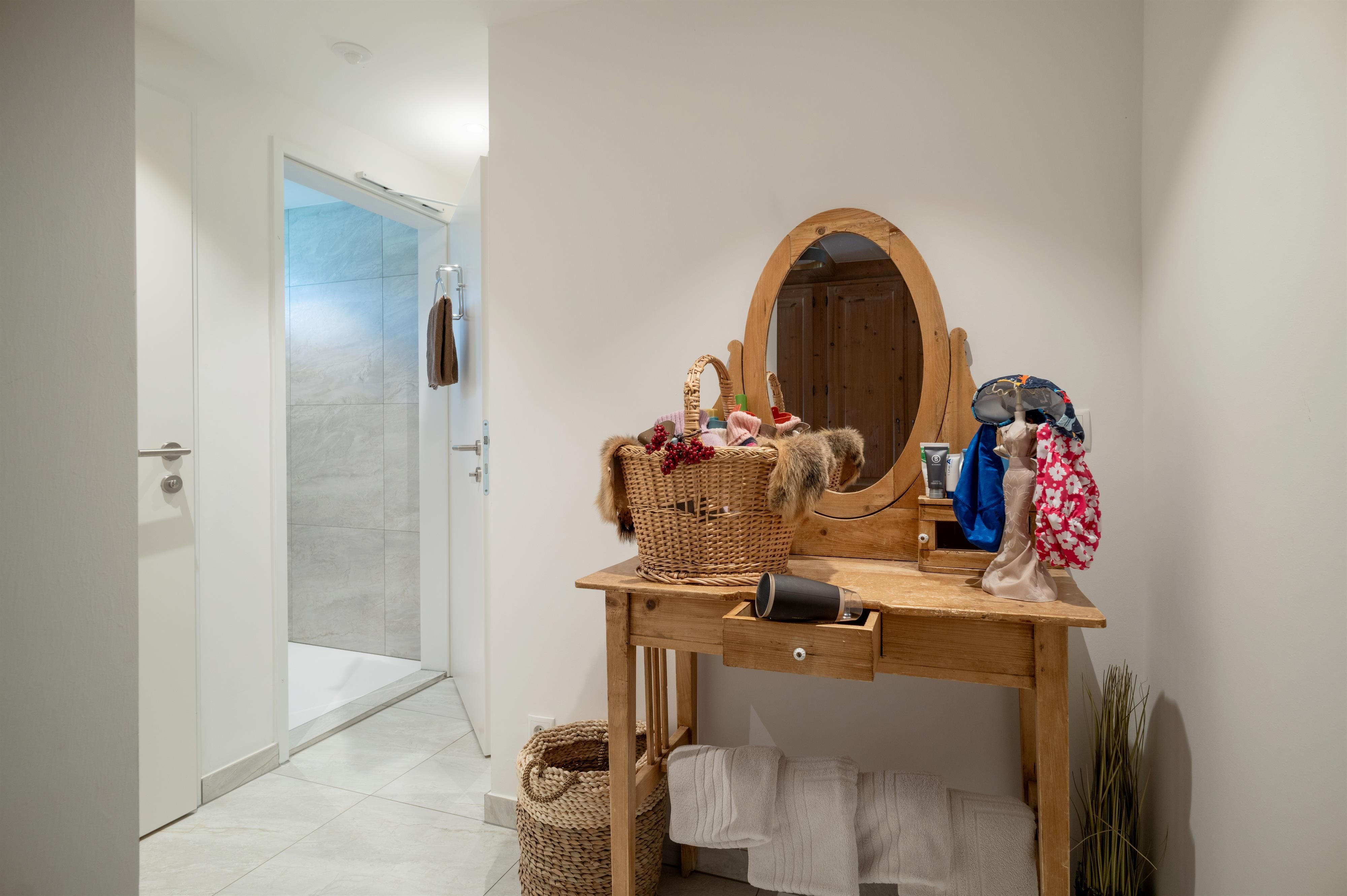 A bright hallway with a wooden desk and a mirror. On the table is a basket with clothes and a plant.