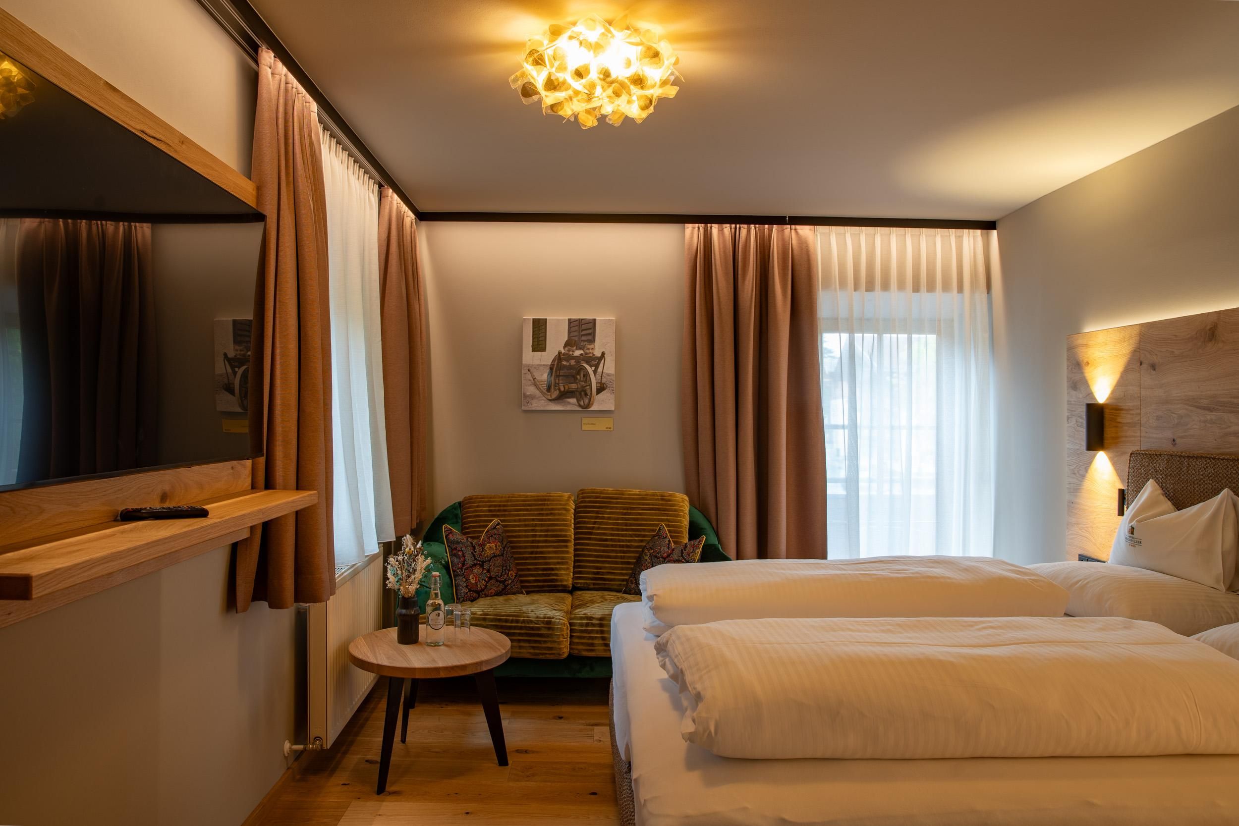 A modern room with two beds and a cozy sofa. Large windows let in plenty of light and create an inviting atmosphere.