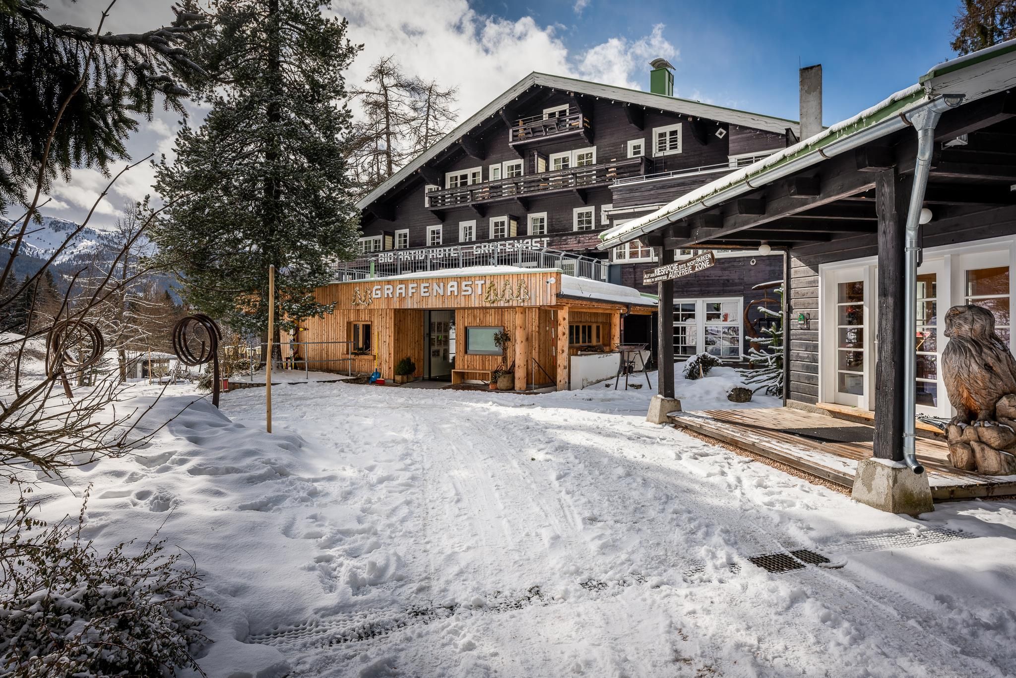 A cozy chalet in the snow, surrounded by trees. The facade is made of wood, and there is an inviting terrace.