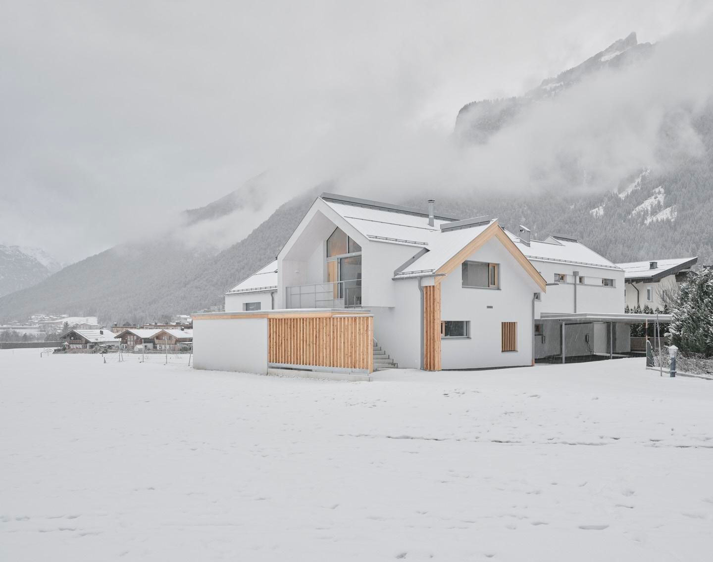 A modern house in a snow-covered landscape. In the background, mountains and clouds can be seen.